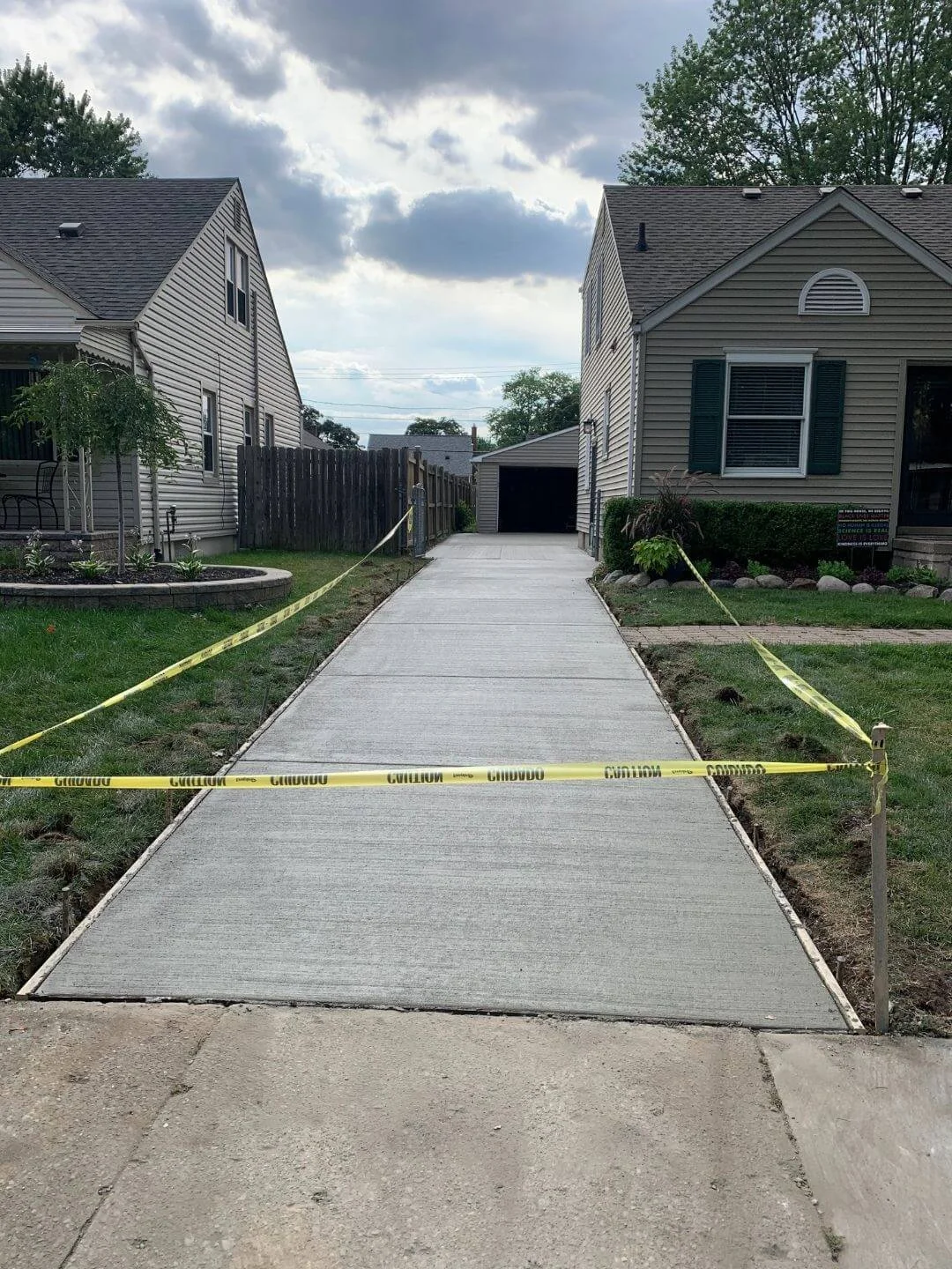 Newly constructed concrete driveway between two houses, blocked off with yellow caution tape.