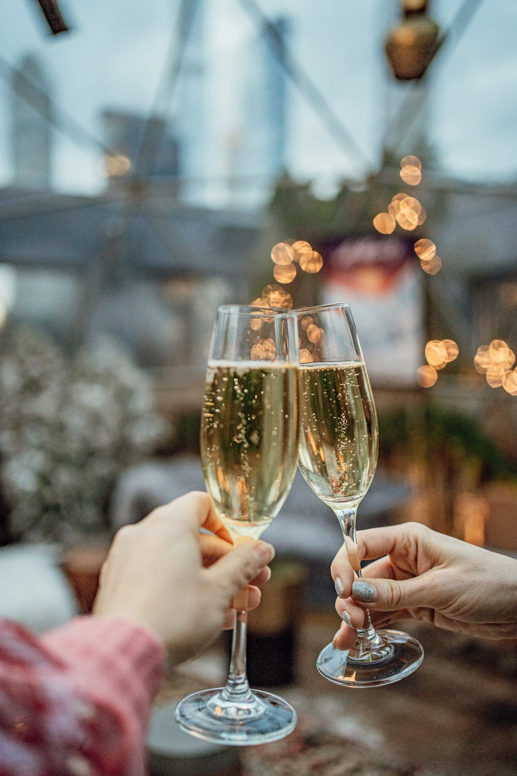 Two people clinking glasses of champagne at a celebration, with blurred festive lights in the background.