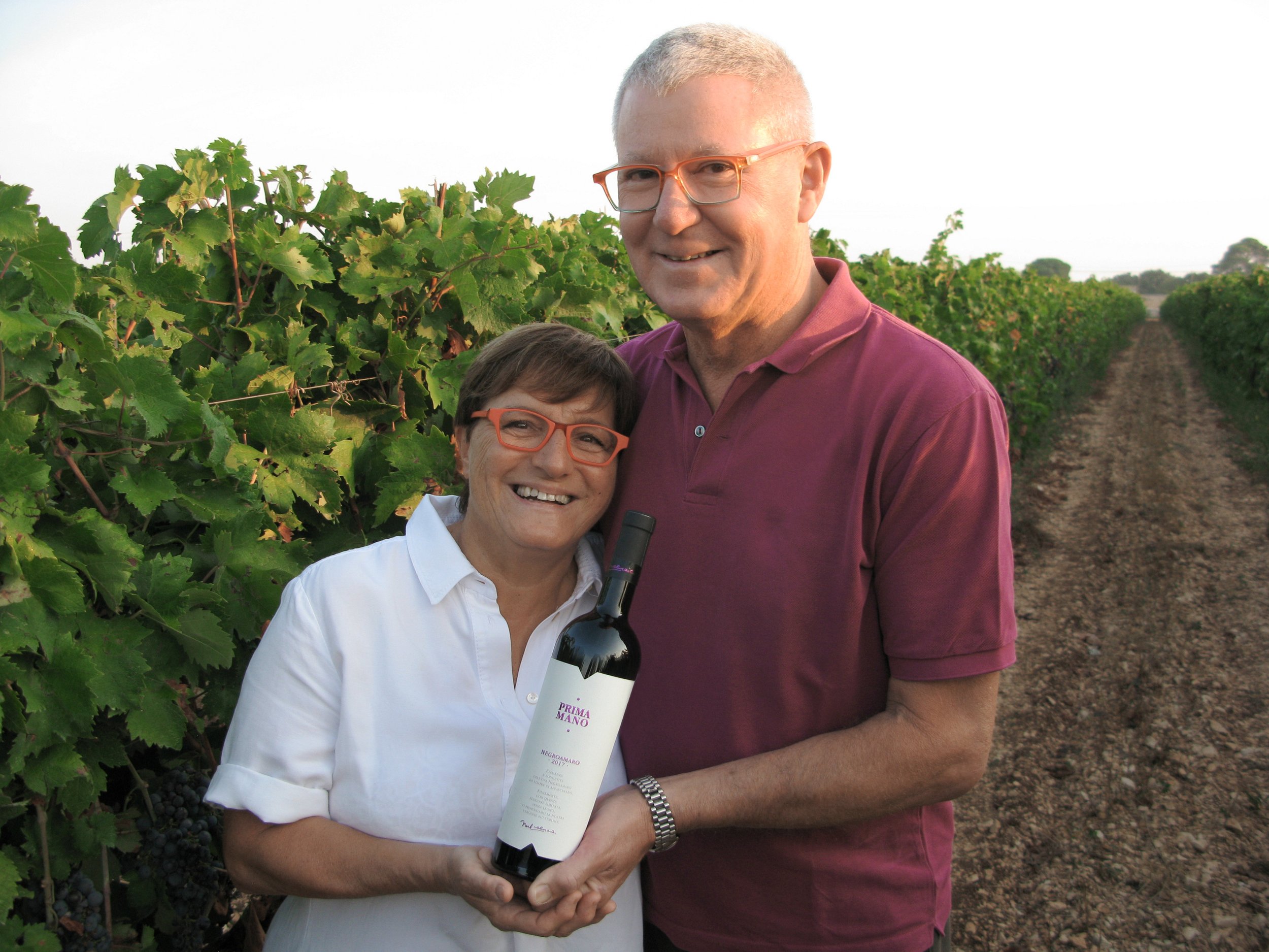 Image showing a couple holding a bottle of red wine the in the middle of a vineyard in Apulia