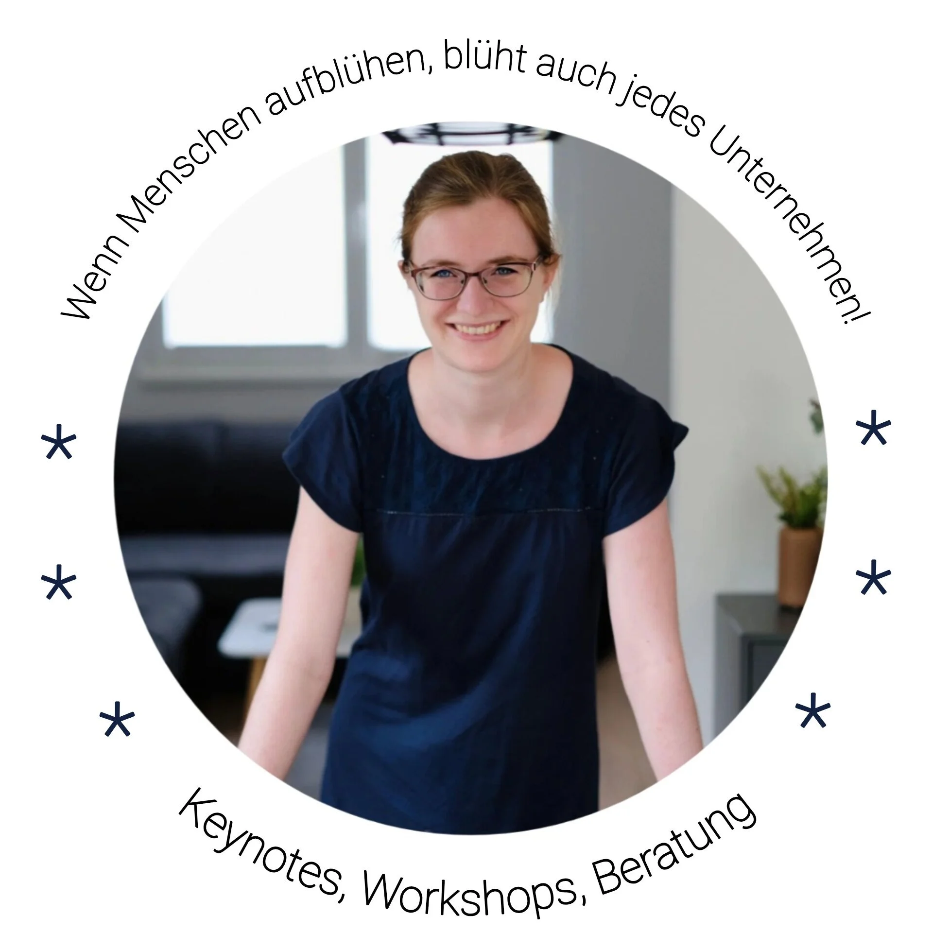 Eine lächelnde junge Frau mit Brille steht in einem hellen Raum, im Hintergrund Fenster und eine Pflanze.