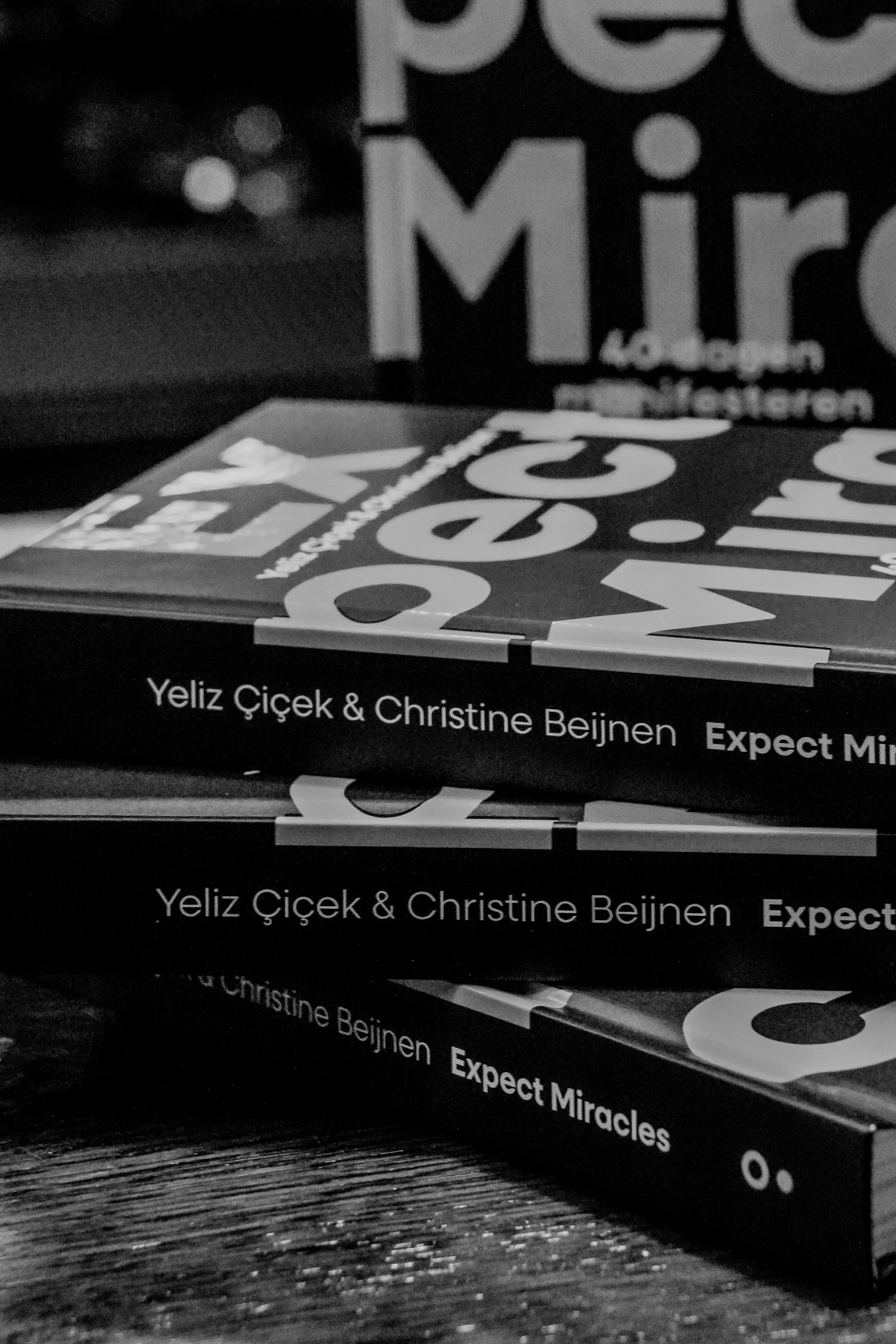 Close-up van boeken met de titel 'Expect Miracles' door Yeliz Çiçek en Christine Beijnen, gestapeld op een houten tafel.