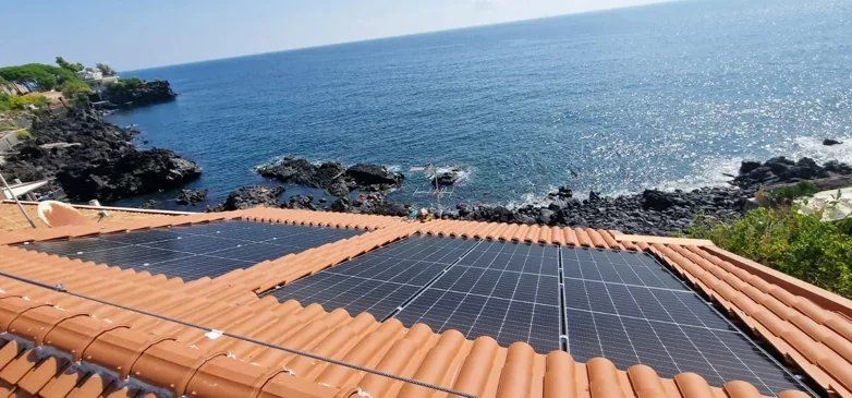 Pannelli solari installati su un tetto con vista su mare e costa rocciosa.