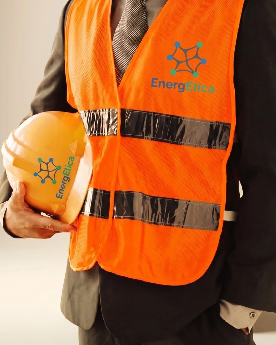 Operaio esperto in piedi con gilet arancione con logo 'EnergEtica' che tiene un casco giallo con lo stesso logo.
