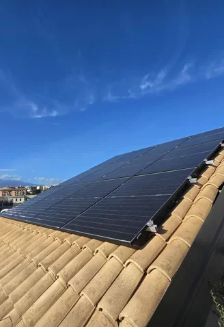 Pannelli solari installati sul tetto di una casa con tegole di terracotta, sotto un cielo blu con alcune nuvole.
