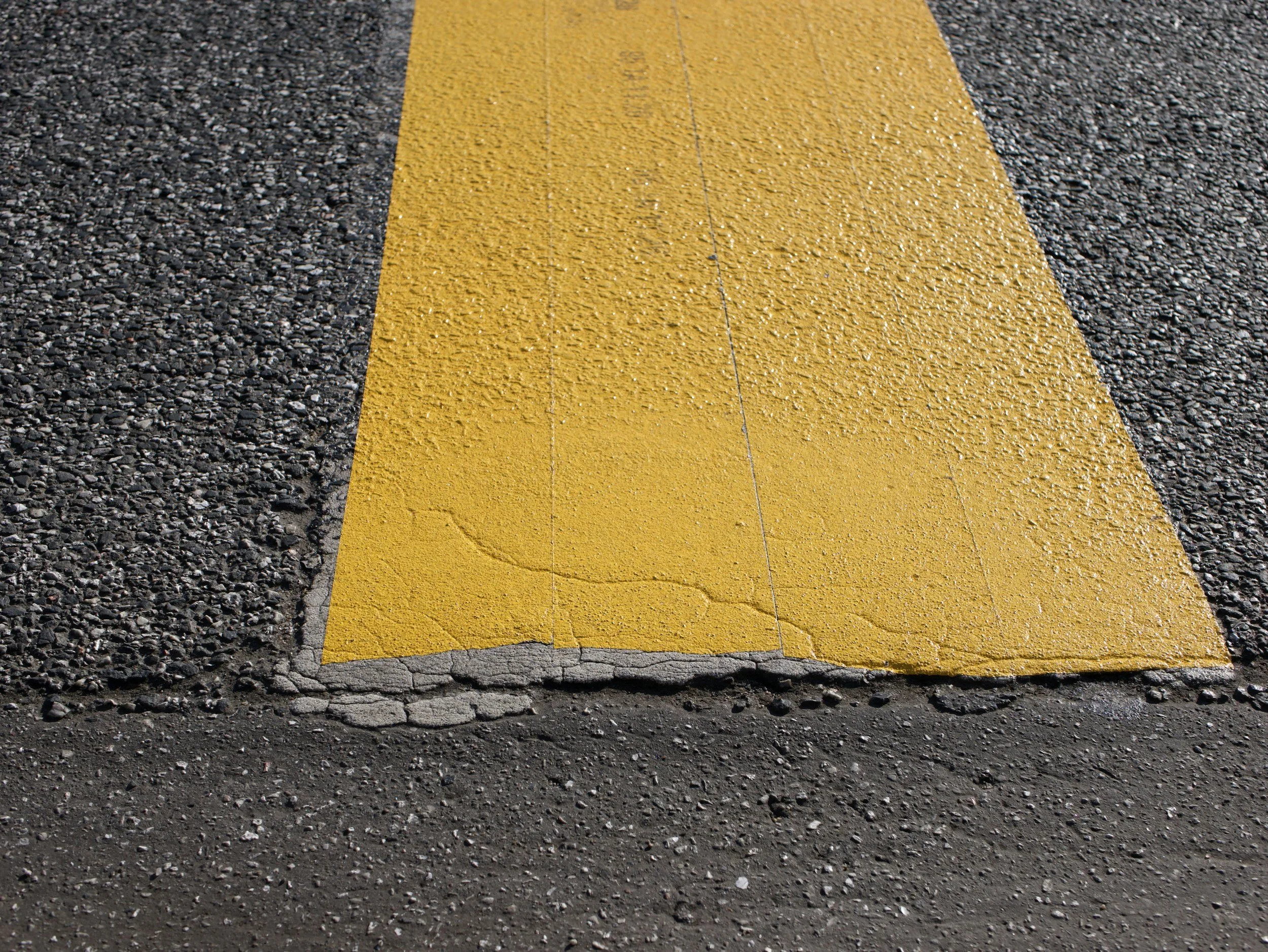 Close-up of a yellow painted crosswalk line on asphalt road with textured gravel surface.
