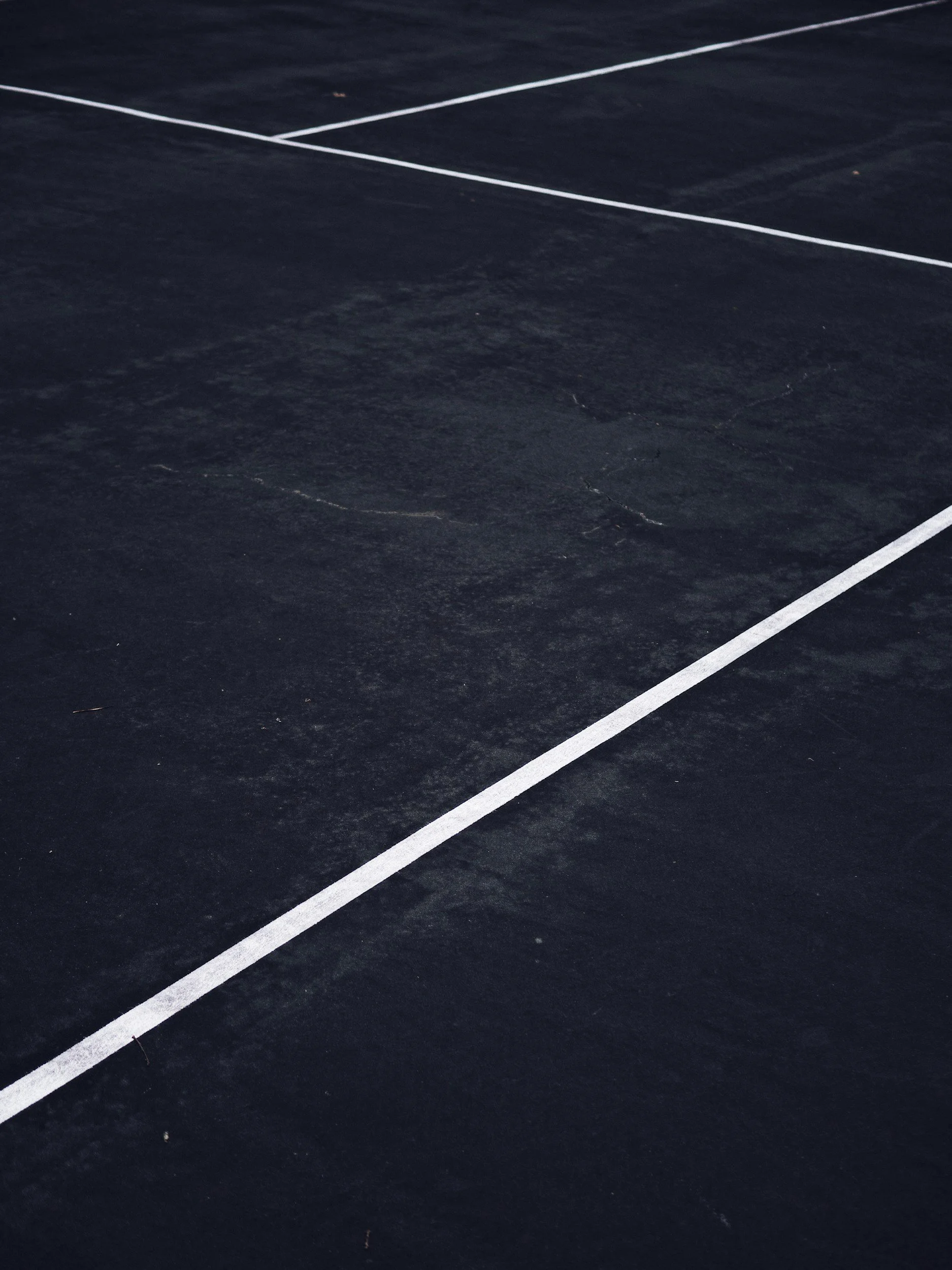 A close-up of a dark asphalt surface with white painted lines, possibly part of a sports court or parking lot.