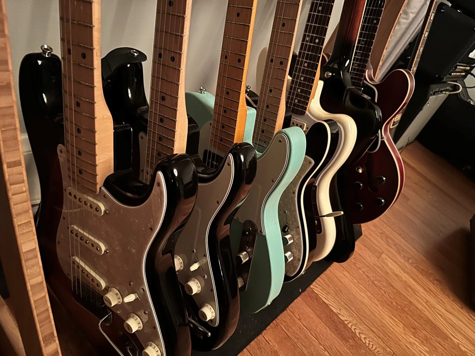 Multiple electric bass guitars with various colors and designs are lined up on a rack in a music room, with a wooden floor.