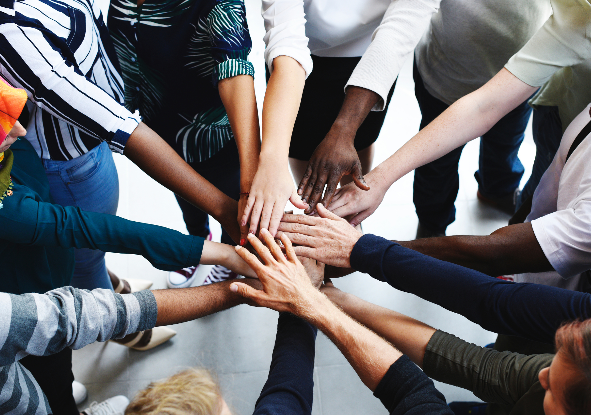 Group of diverse people with their hands together in the center, showing teamwork and unity.