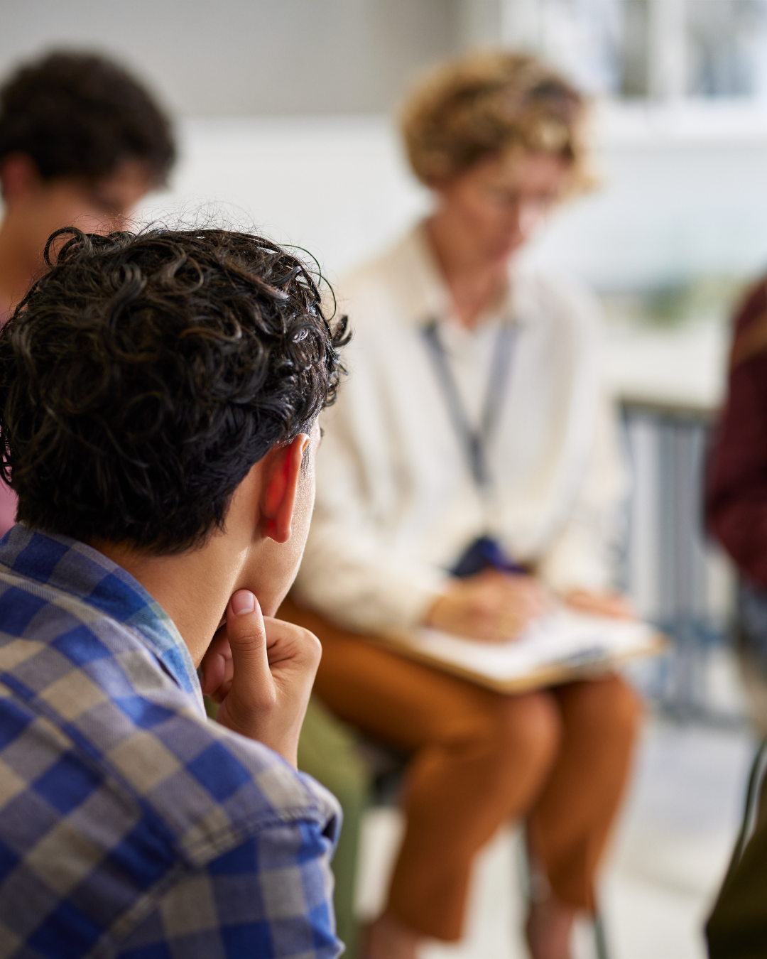 Person with curly hair listening to a woman with glasses speaking in an indoor setting.