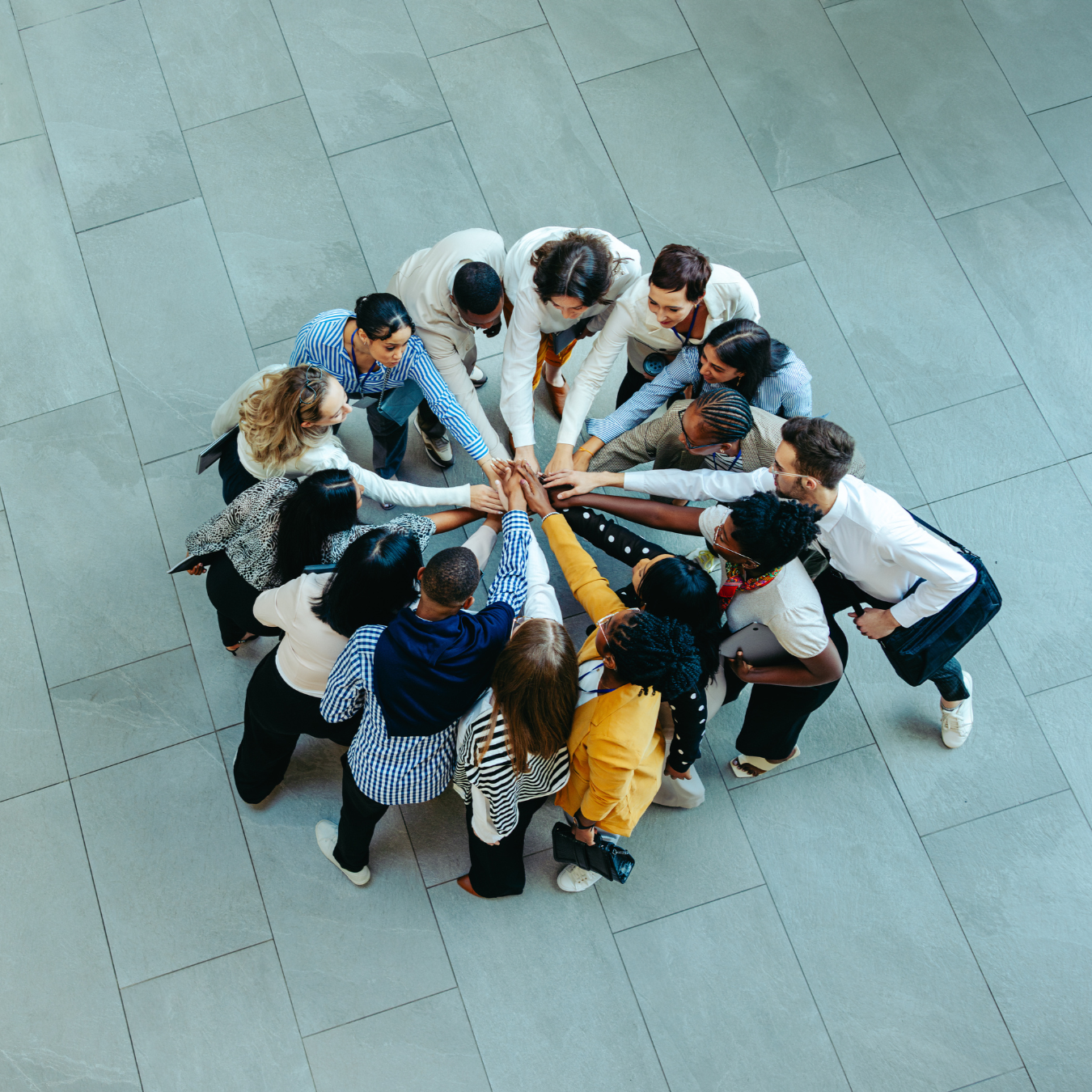 A diverse group of people standing in a circle, putting their hands together in the center as a symbol of unity and teamwork.