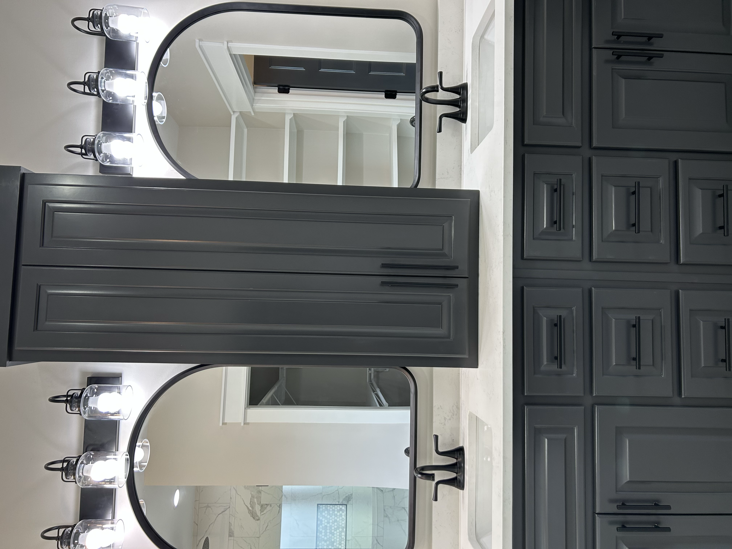 Bathroom vanity mirror with lights and black faucet, dark cabinets, and white countertop.