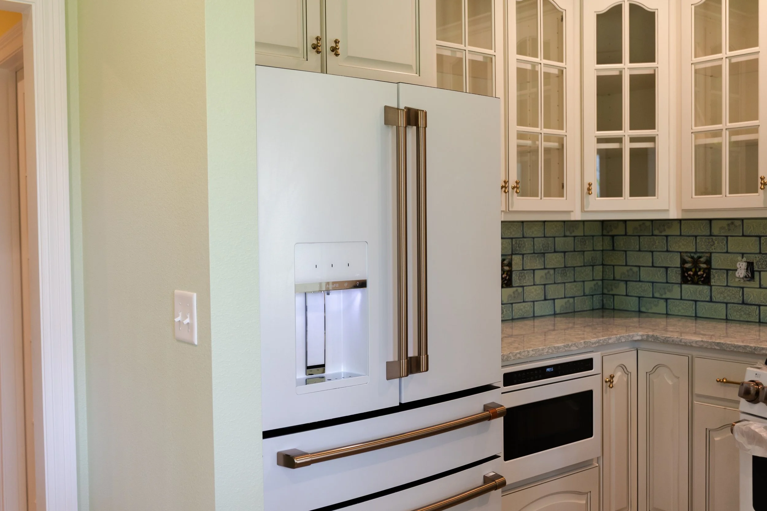 Kitchen with white cabinets, an electric oven, a refrigerator with gold handles, and a tiled backsplash with decorative tiles.