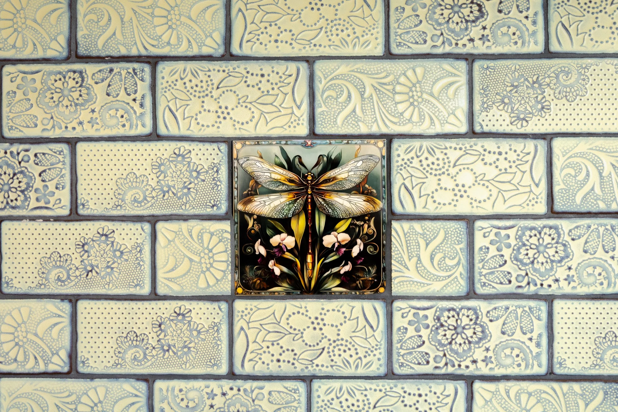 A mosaic wall with a decorative tile featuring a dragonfly and floral design.