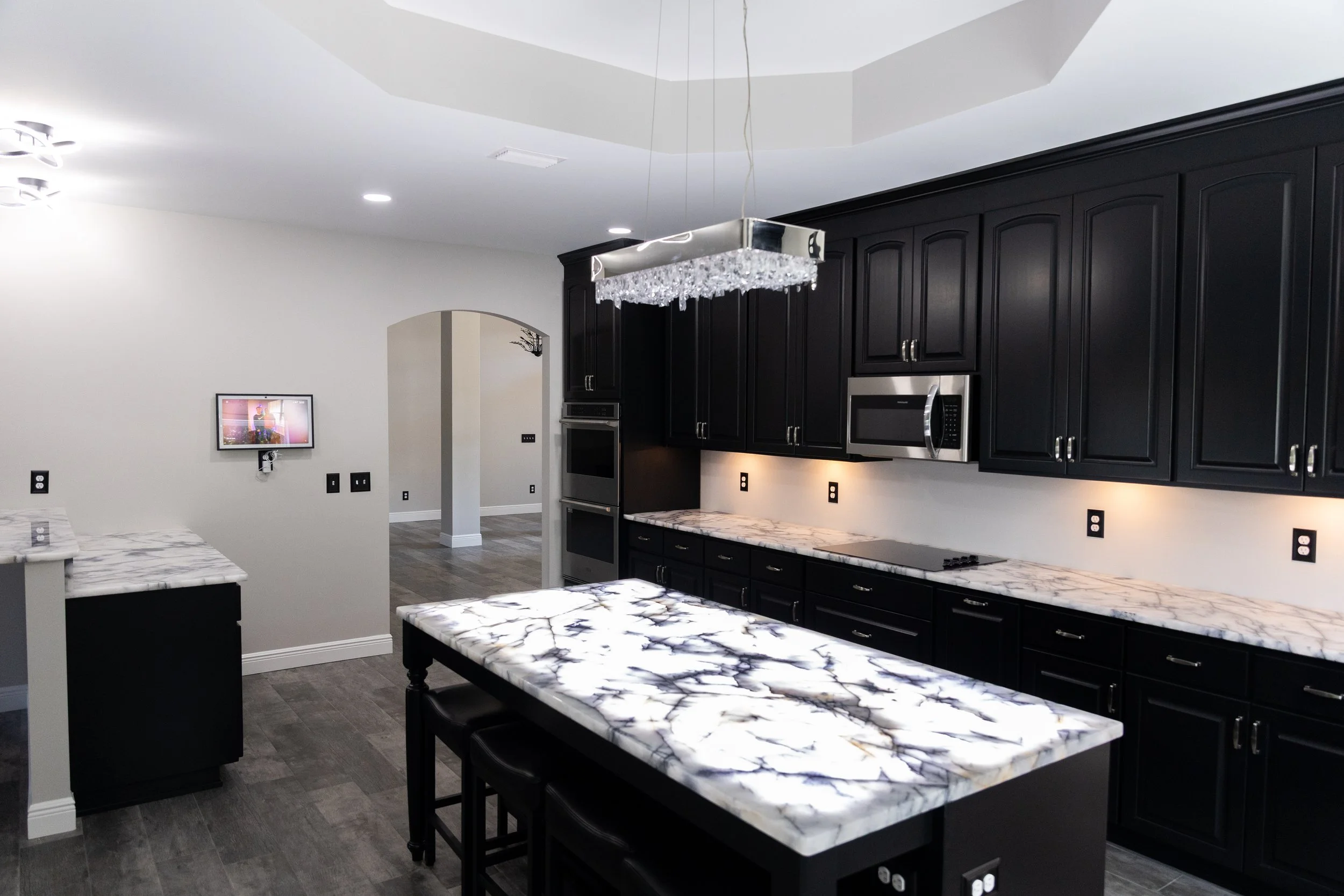 Modern kitchen with black cabinets, marble countertops, and a chandelier overhead.