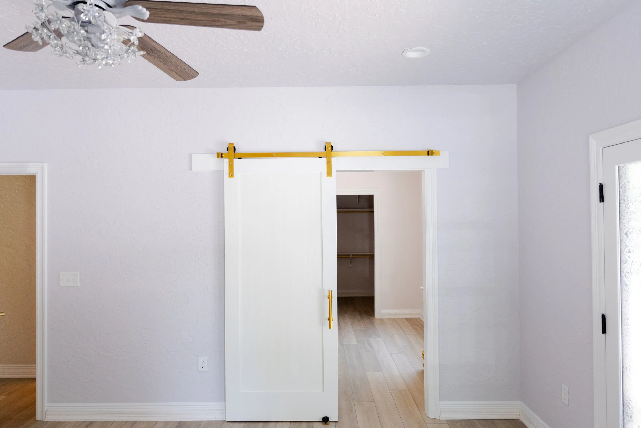 Interior room with door, white walls, ceiling fan, and a sliding barn door on a yellow rail.