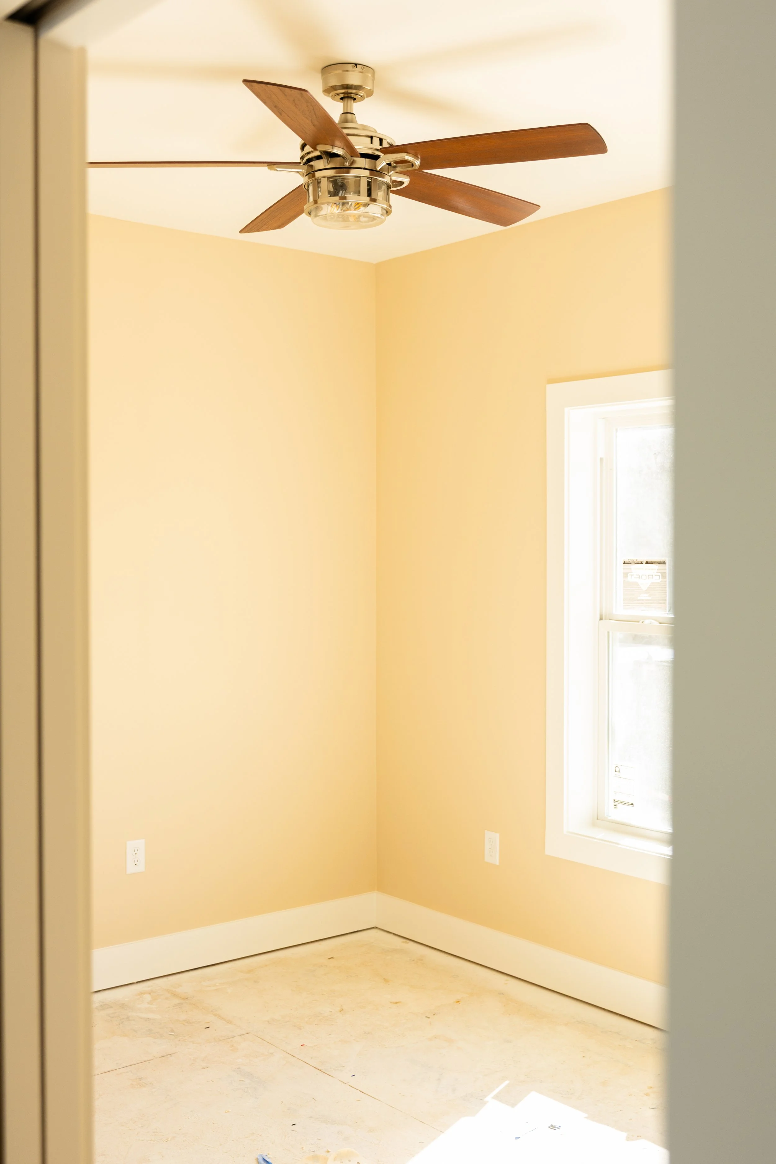 Empty room with beige walls, white window trim, and electrical outlets, under natural light.