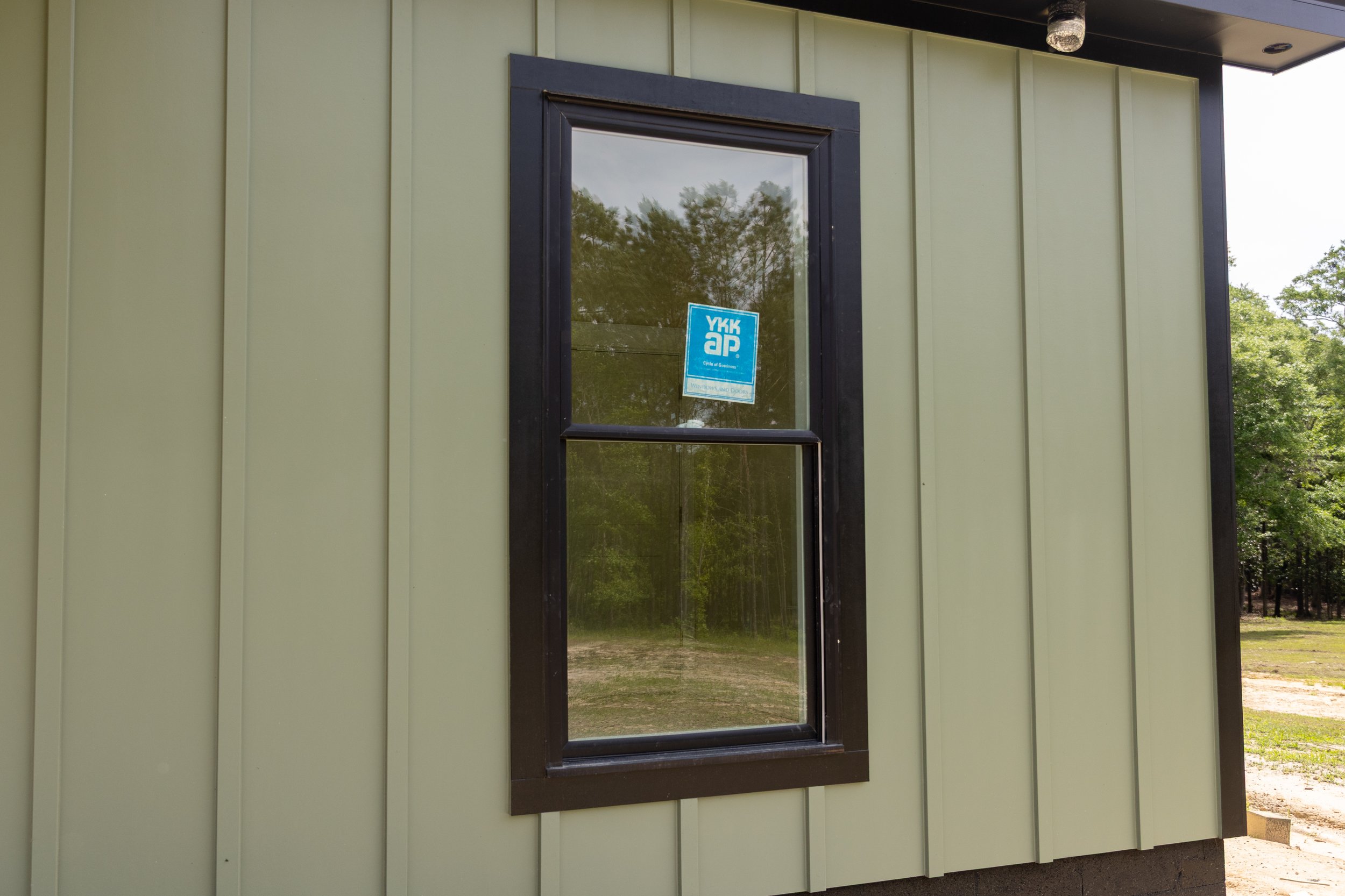 A beige building exterior with a black framed window, reflecting trees and sky, and a blue sticker on the window reading 'YKK AP'.