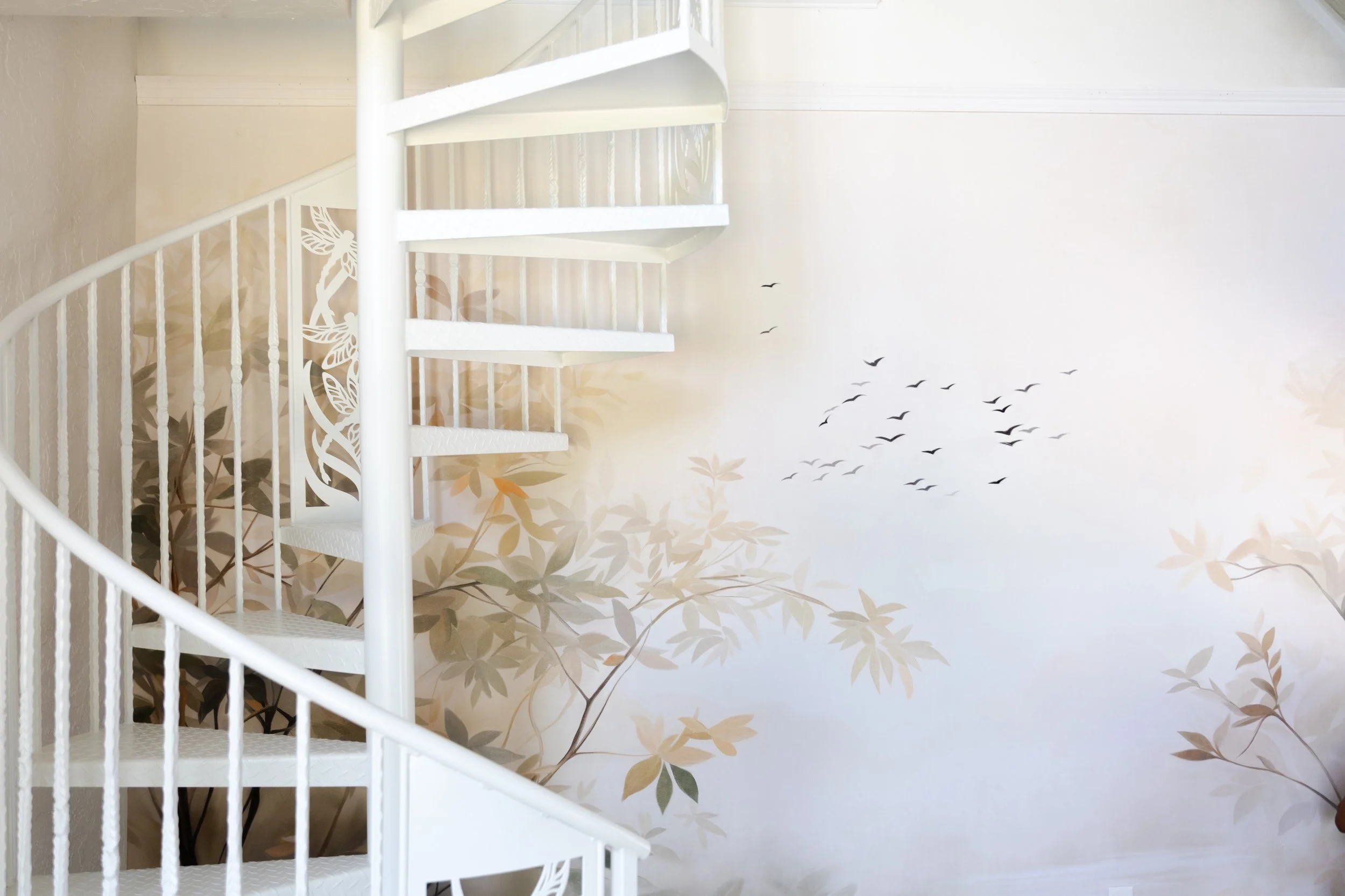 White spiral staircase next to a beige floral mural wall with birds flying.