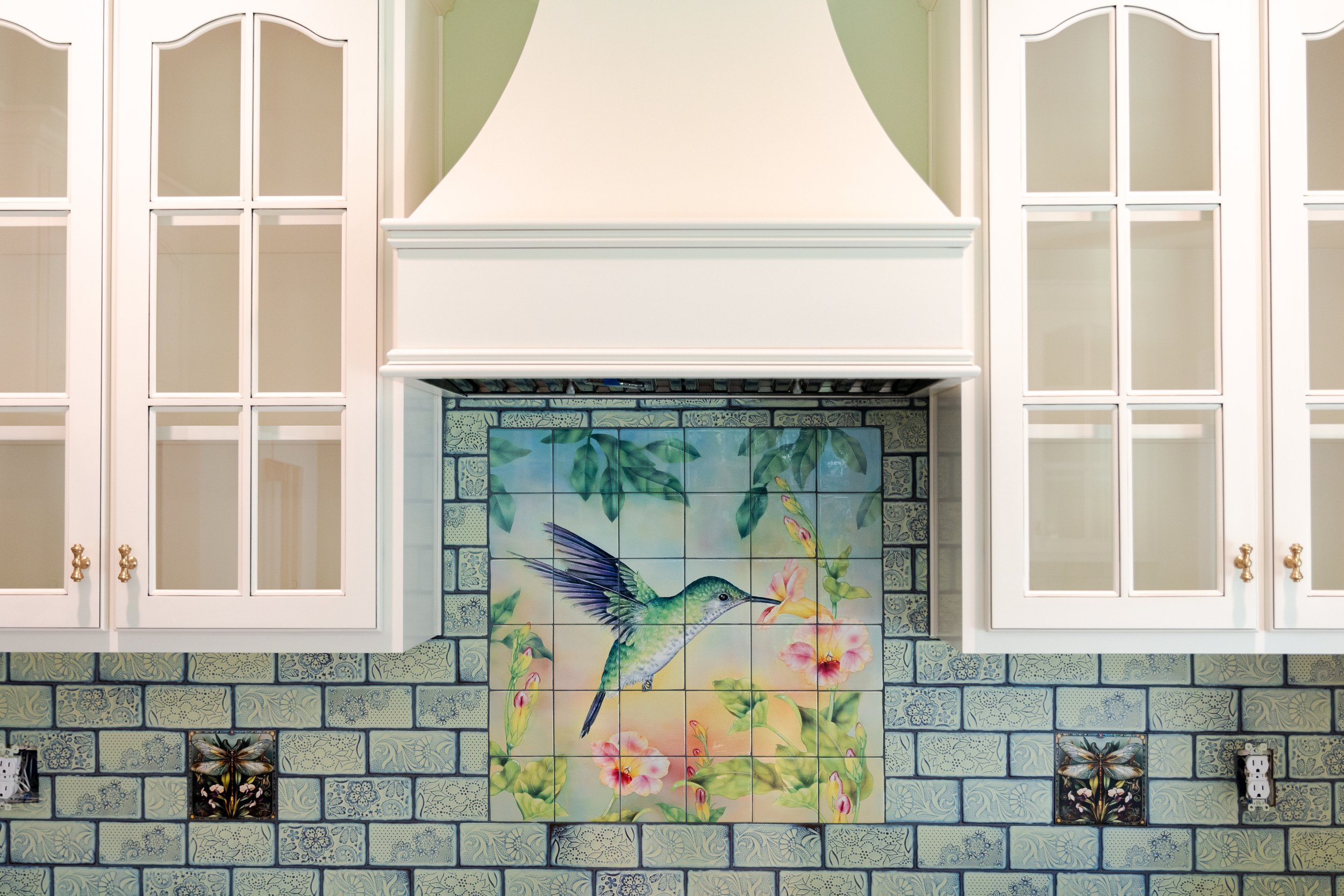 Kitchen backsplash with decorative tiles featuring a hummingbird and flowers, surrounded by white cabinetry.