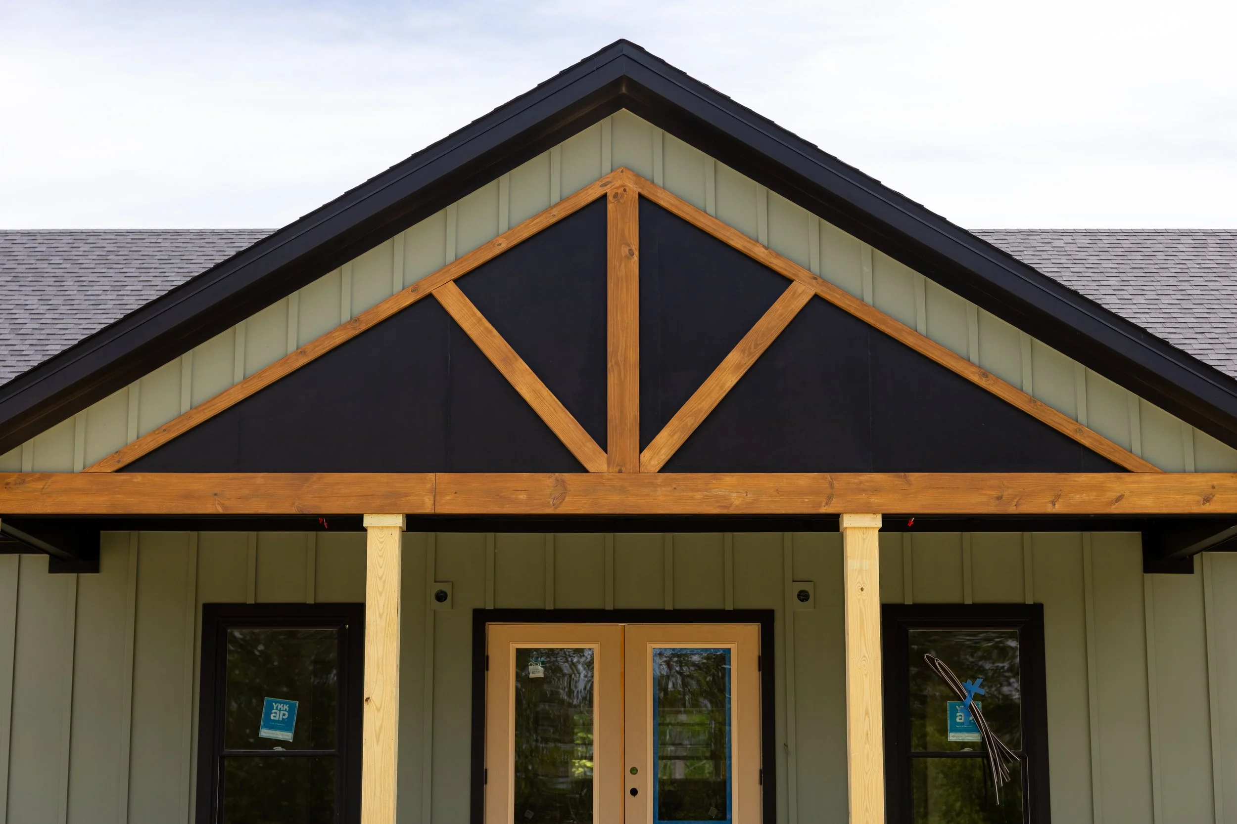 Front view of a house under construction with a gable roof, vertical siding, and exposed wooden framing around the entryway.
