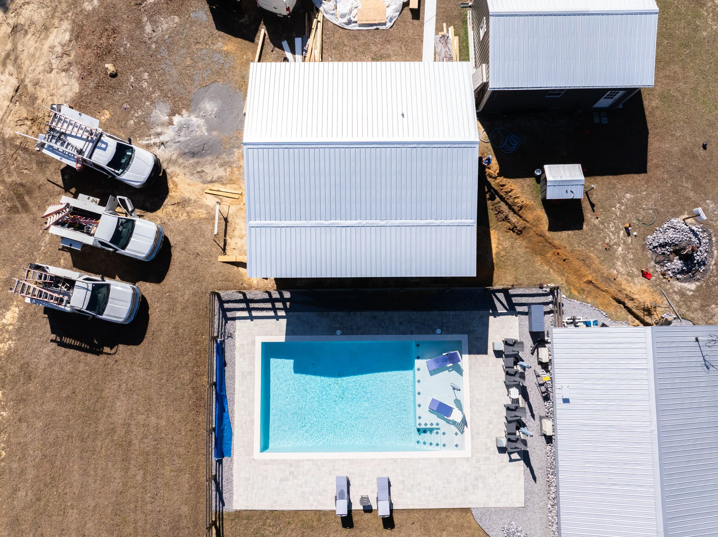 Aerial view of a house with a swimming pool in the backyard, and construction work happening nearby with construction vehicles and materials.