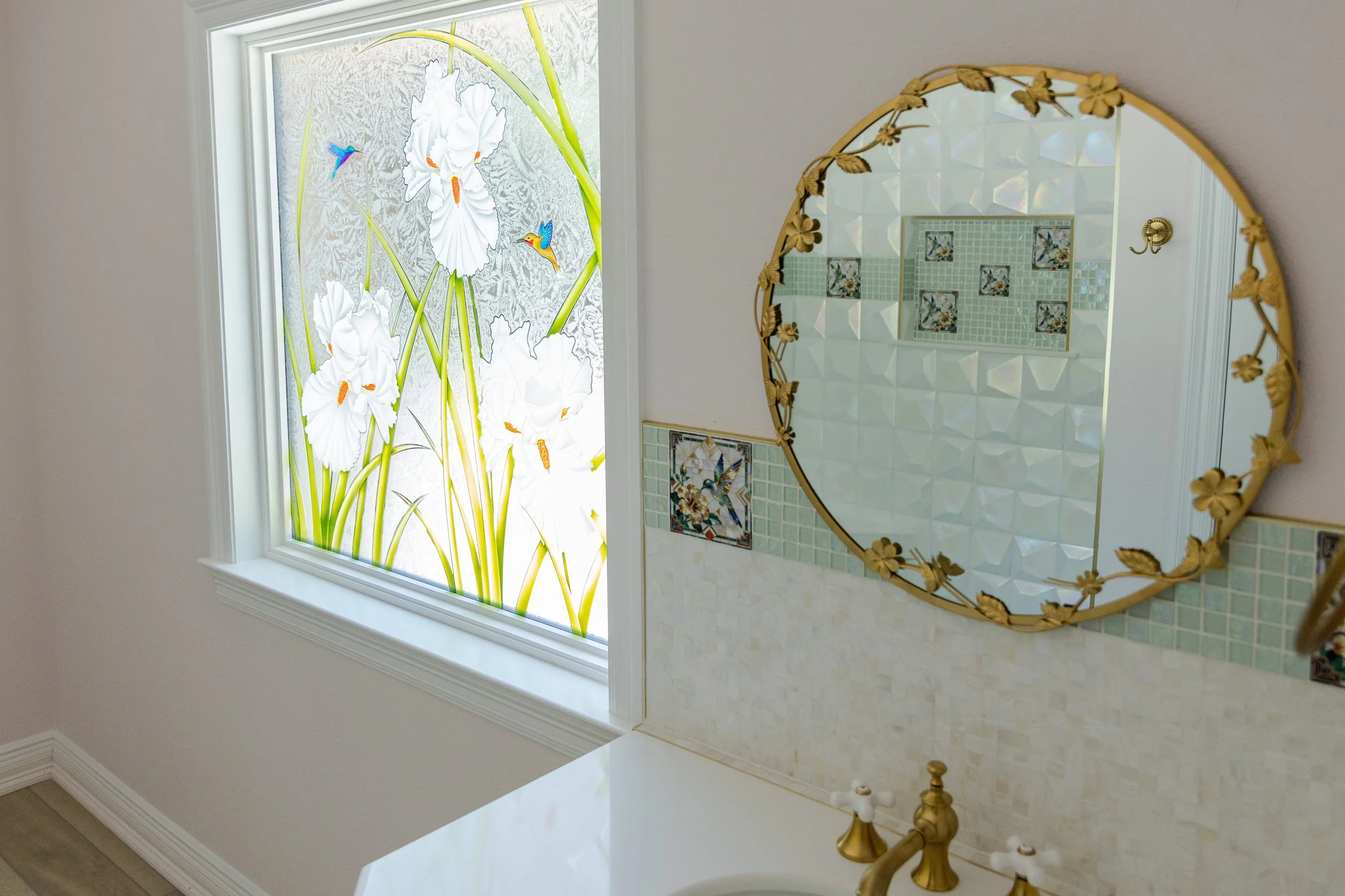 Decorative window with floral and hummingbird design in a room with a mirror and tiled wall.