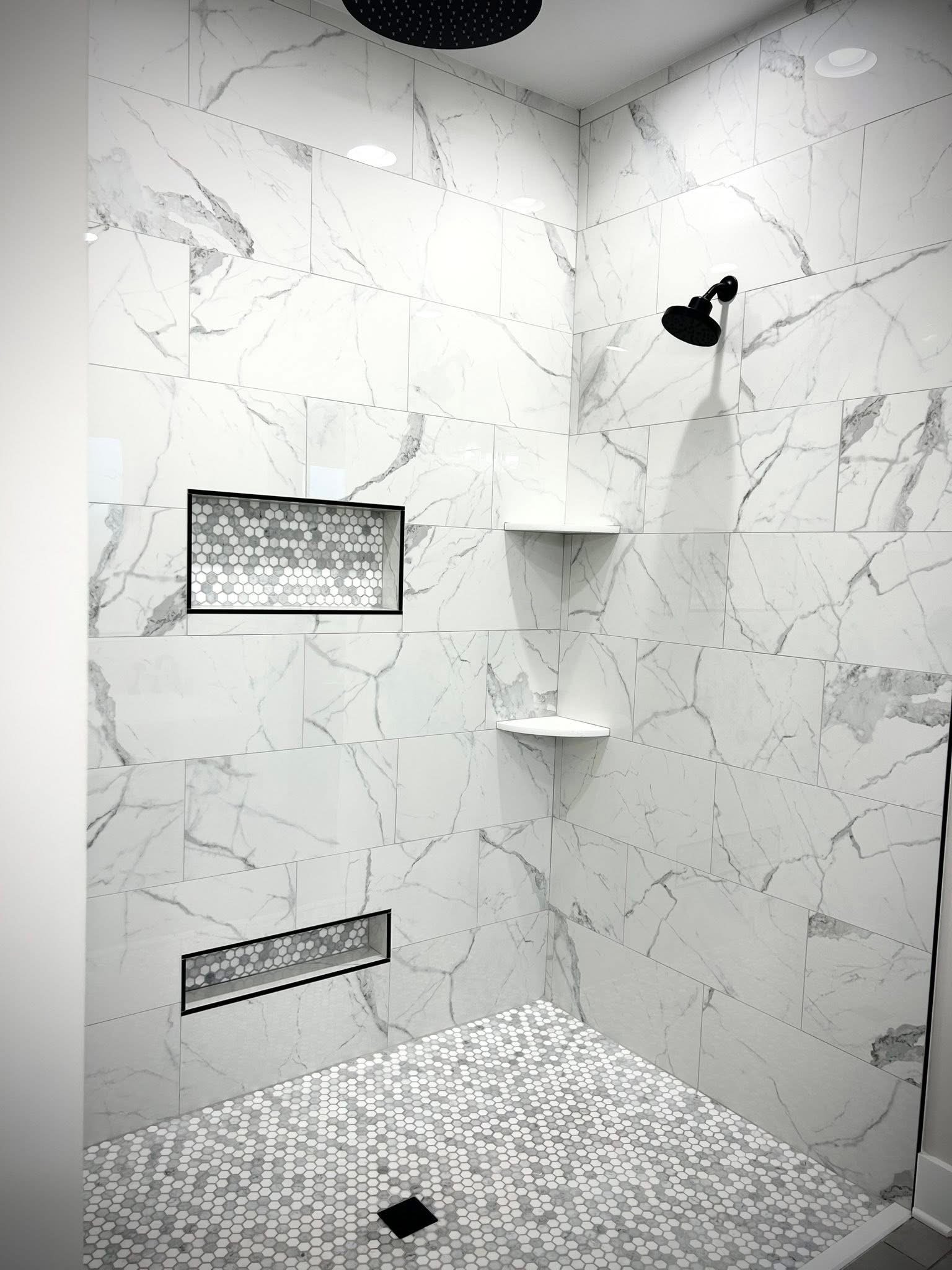 Modern white marble tiled shower with black fixtures, built-in corner shelves, a hexagonal tile floor, and a small hexagonal tiled niche with a black border.