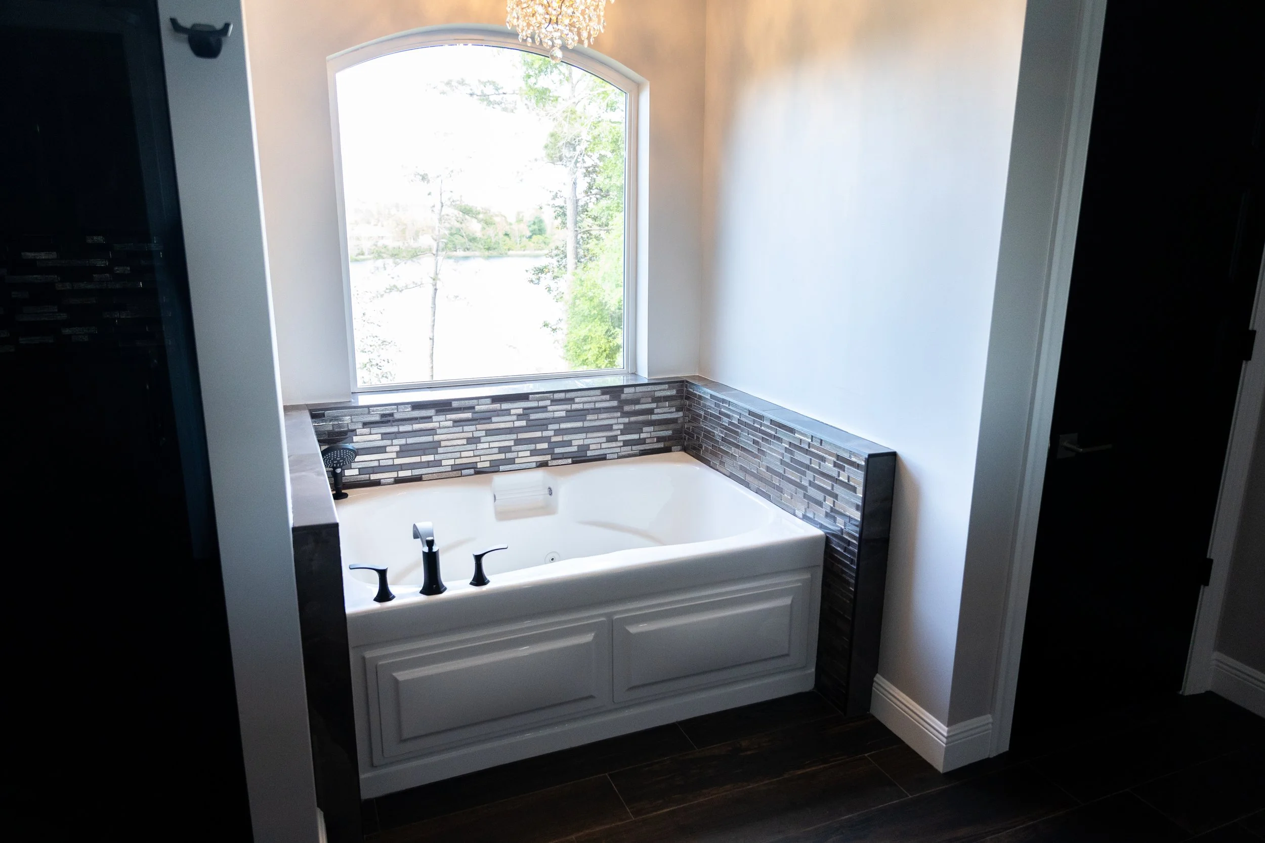 Bathroom with a large window, chandelier, and a bathtub with a brick-patterned surround.