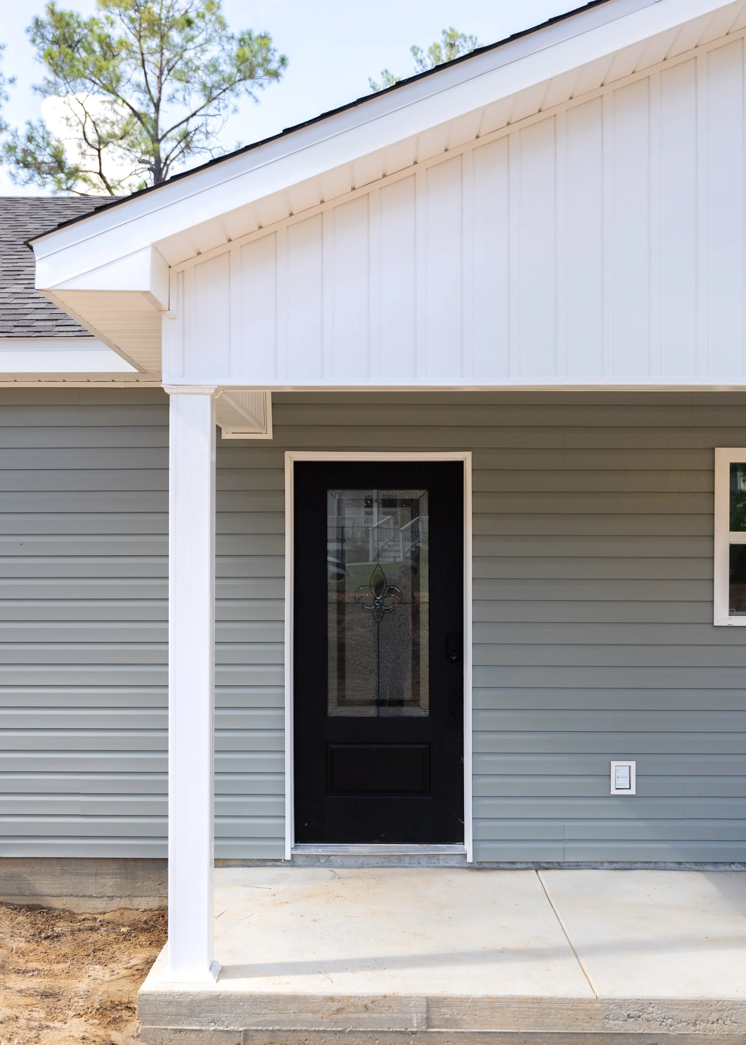 Front porch of a house with gray siding, a black door with a glass window, and a white post supporting the roof over the porch.