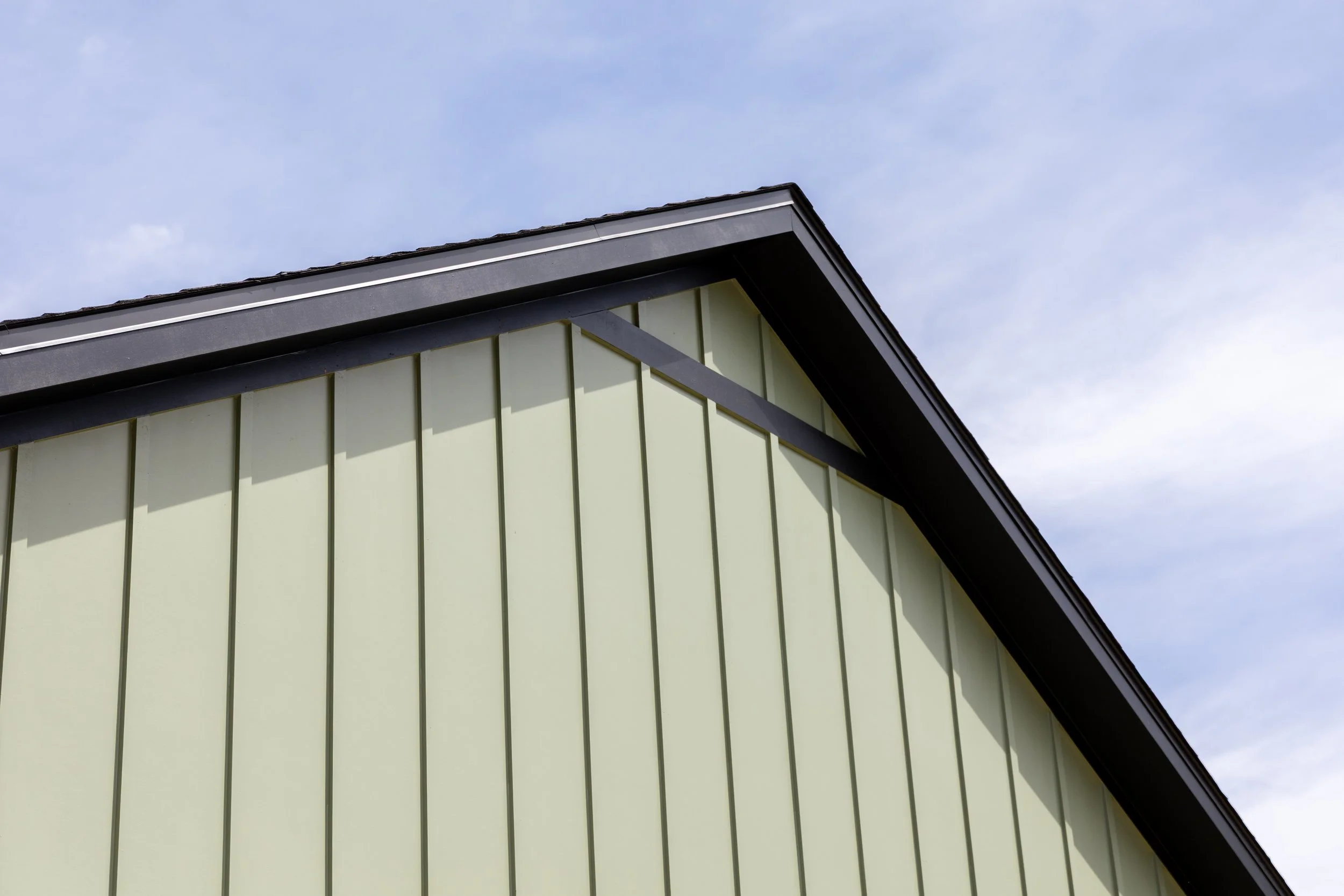 Close-up of the corner of a house with yellow siding, black roof trim, and a cloudy sky background.
