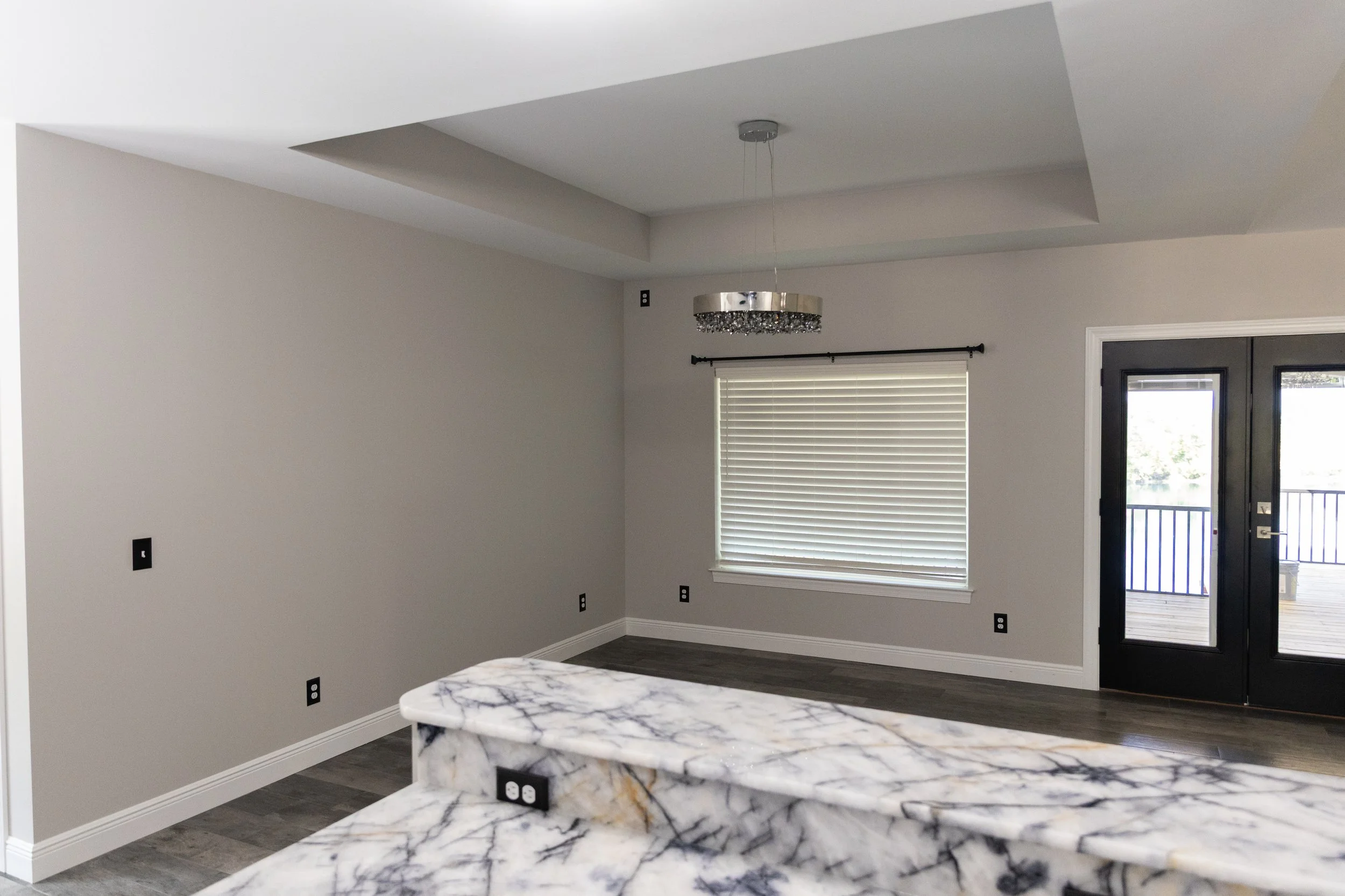 Interior of a modern room with a marble kitchen island, gray walls, a window with blinds, a door with glass, and a ceiling light fixture.