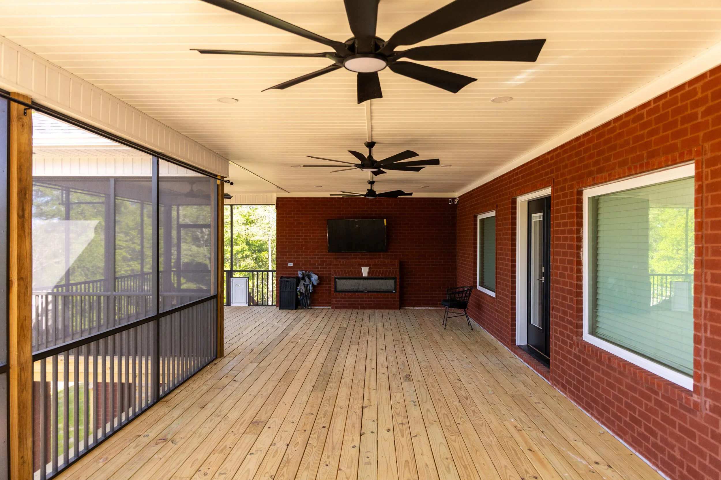 Covered porch with ceiling fans, brick wall, sliding glass doors, and wooden flooring.