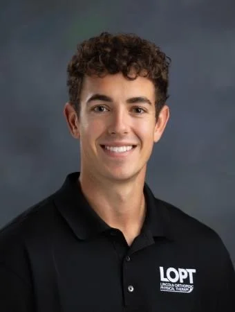A young man with curly brown hair, smiling, wearing a black polo shirt with a logo that reads 'LOPT' and 'Lincoln Orthopedic Physical Therapy'.