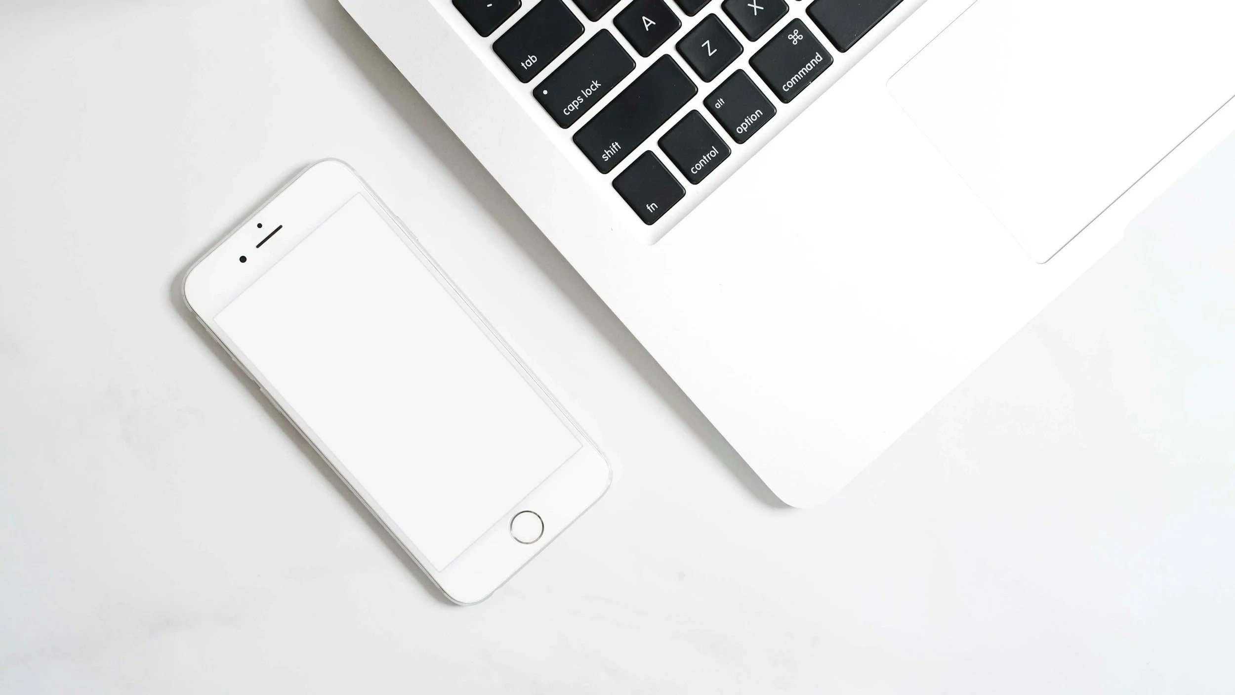 Close-up view of a white smartphone and a silver laptop keyboard on a white surface.