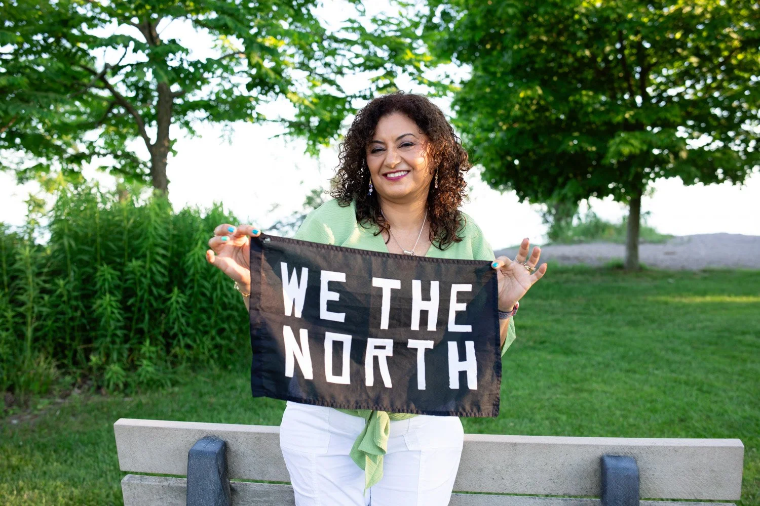 Lucy Shenouda smiling at camera holding a 'We The North' Banner