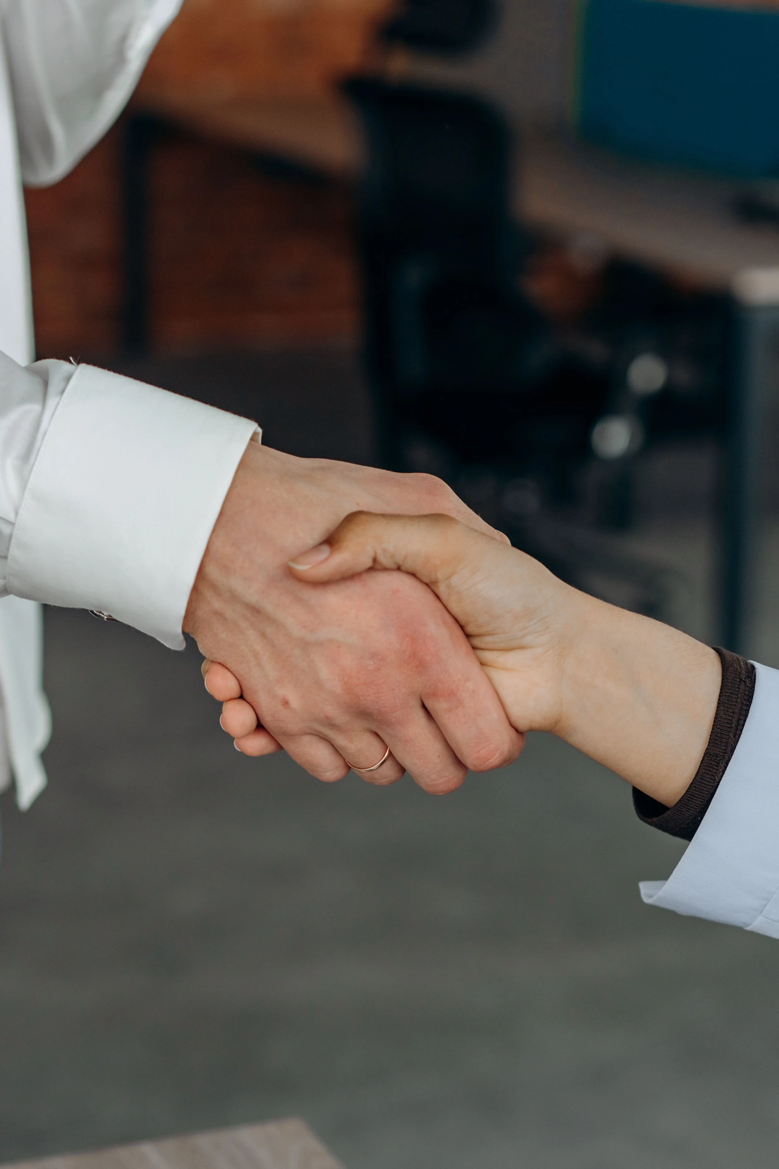 Two individuals shaking hands, one wearing a white shirt and the other wearing a dark long sleeve shirt.