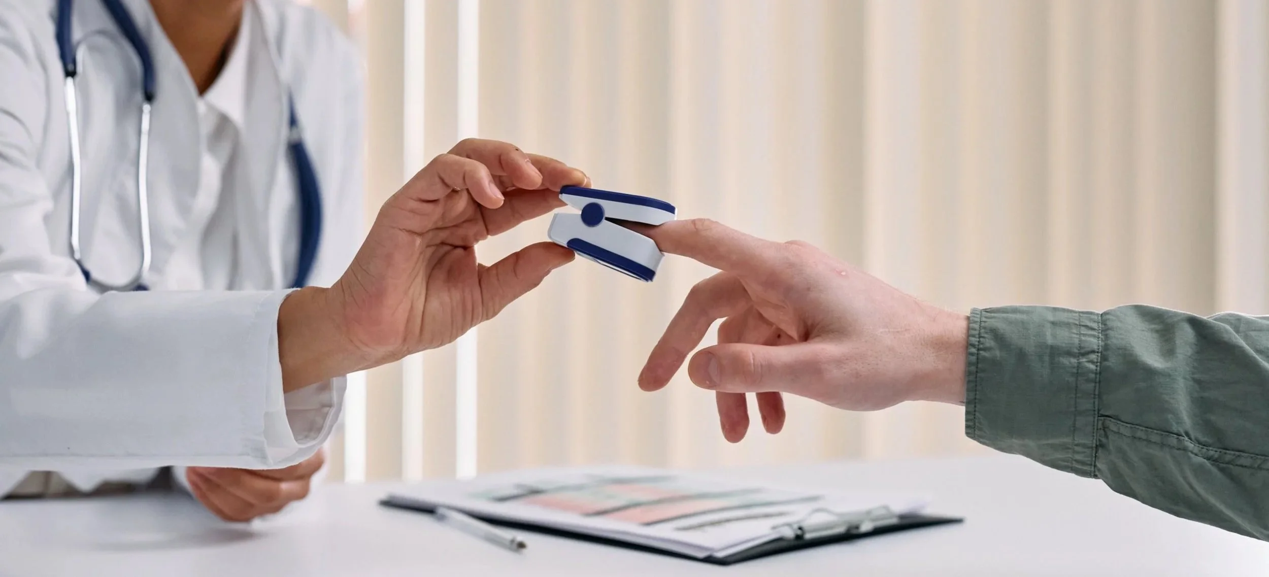 A healthcare professional in a white coat using a pulse oximeter on a patient's finger.