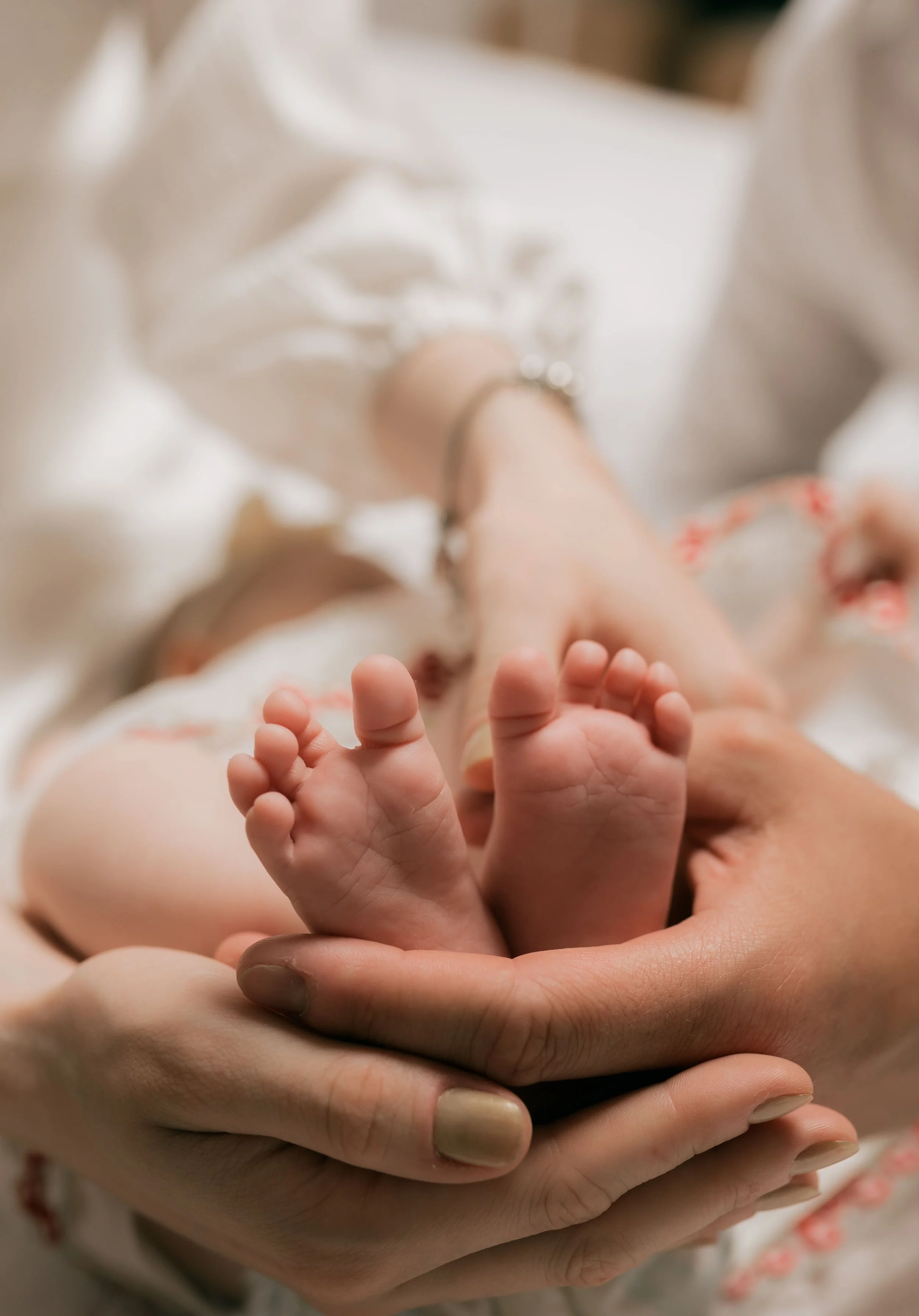 A close-up of a person holding a baby's foot with both hands, with the baby lying on a white surface.