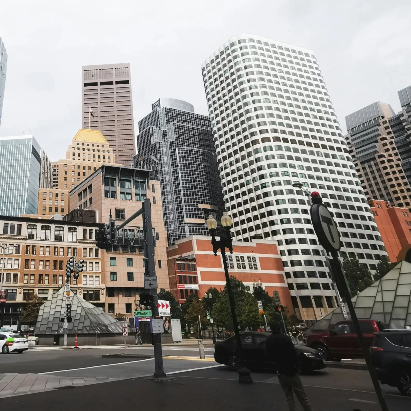 Cityscape of tall modern office buildings with pedestrians and vehicles on the street, overcast sky, urban area.