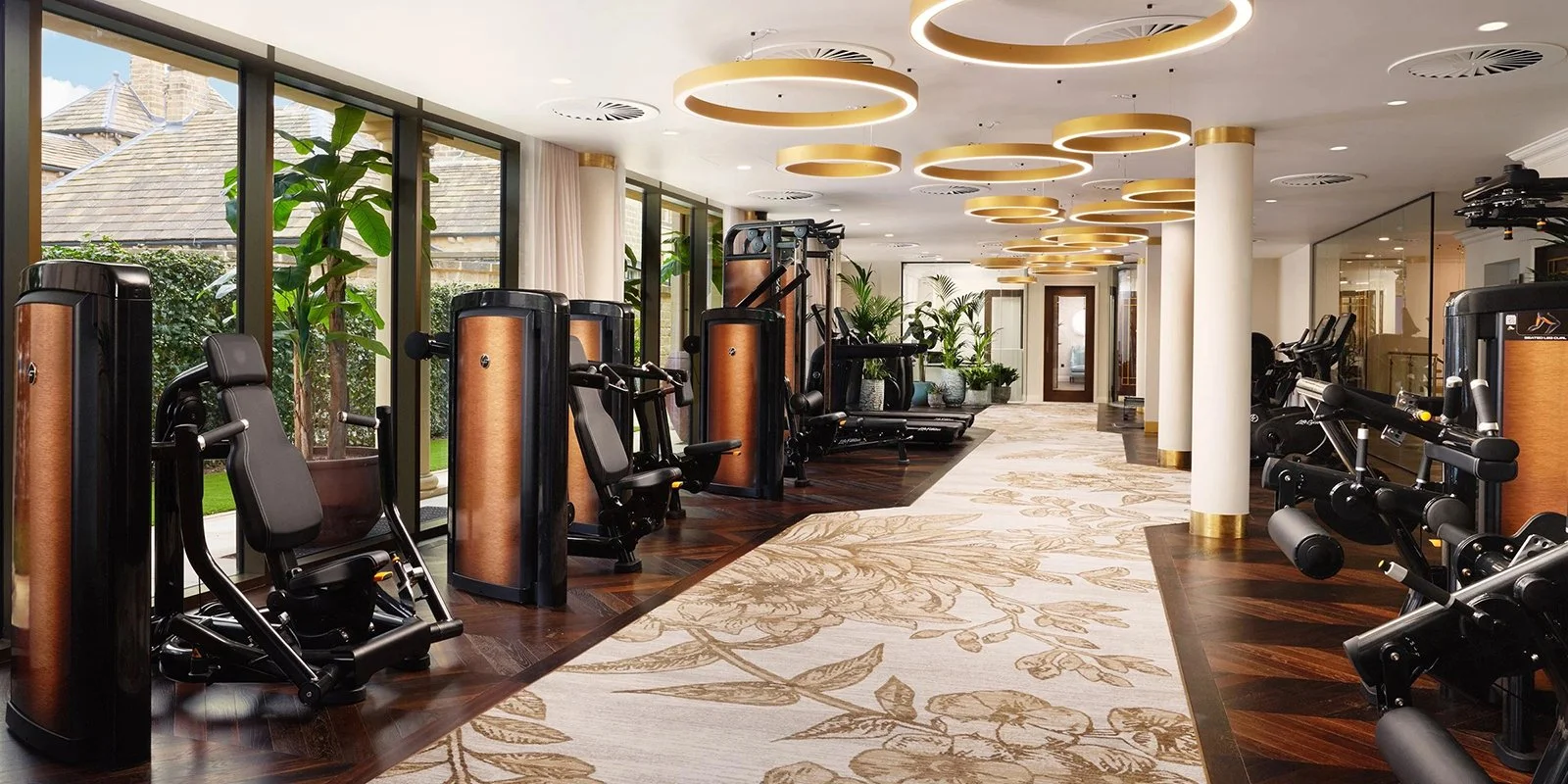 Well-lit gym with large windows, modern workout equipment, and decorative ceiling lights in a stylish fitness center.