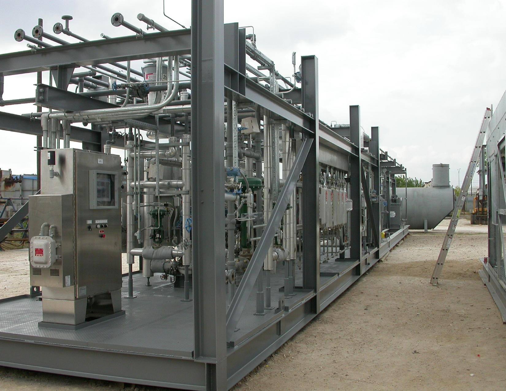 Large industrial equipment with pipes, valves, and control panels at an outdoor installation site.