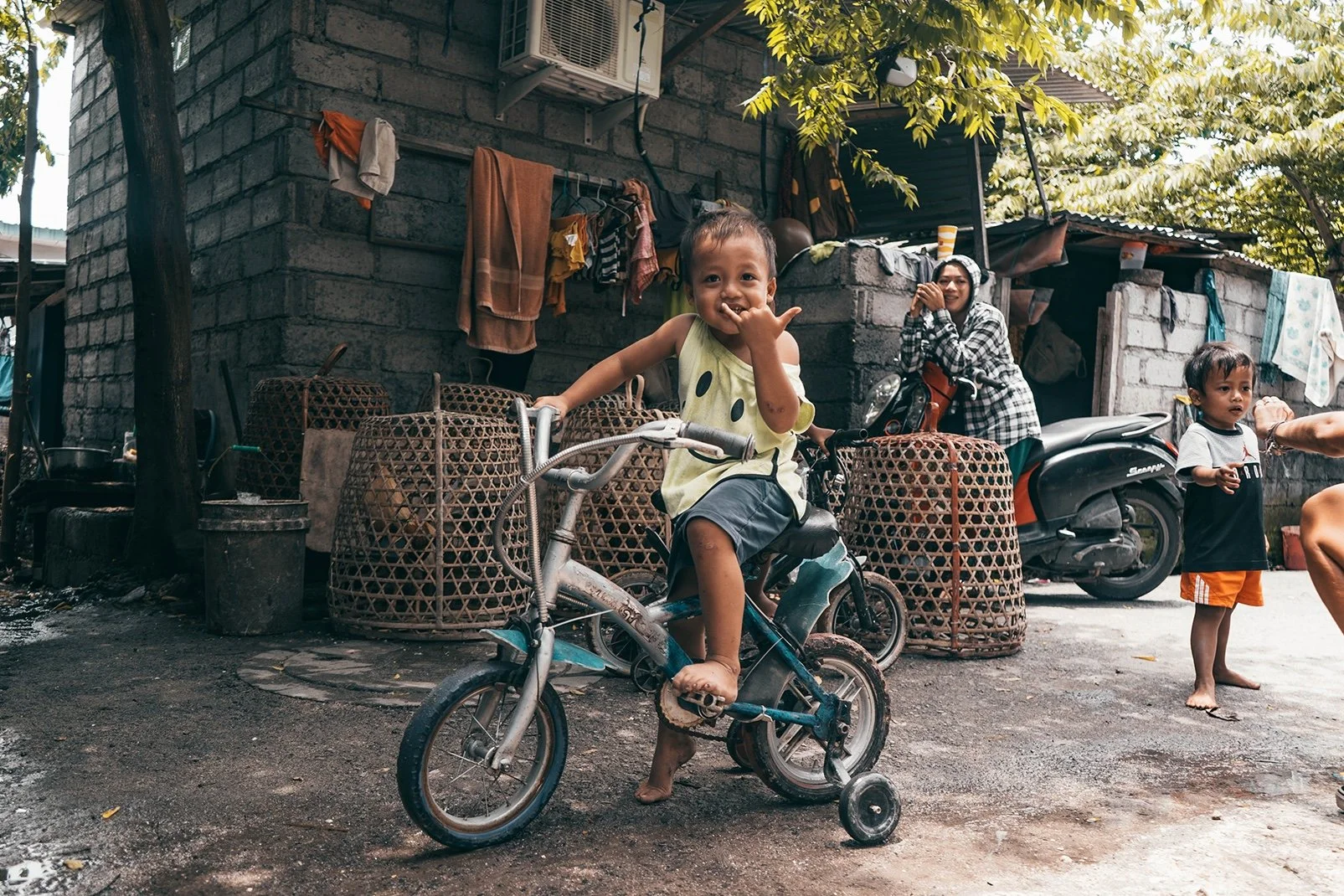 alt="A child in an Indonesian community smiling and giving a peace sign after EXC International delivered meals to local families"