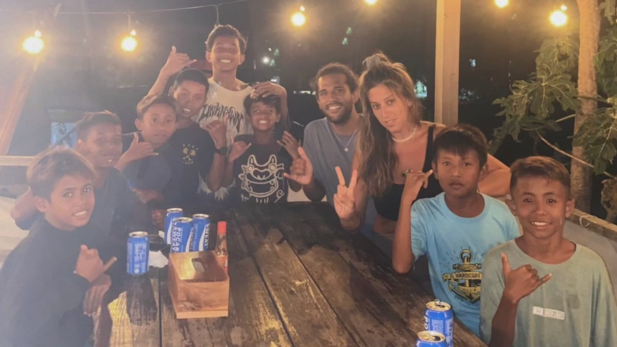 alt="EXC International founders with local surfer kids at Fathma's in Lakey Peak, Indonesia, after donating surfboards to give children access to surfing and a path to professional sponsorship"