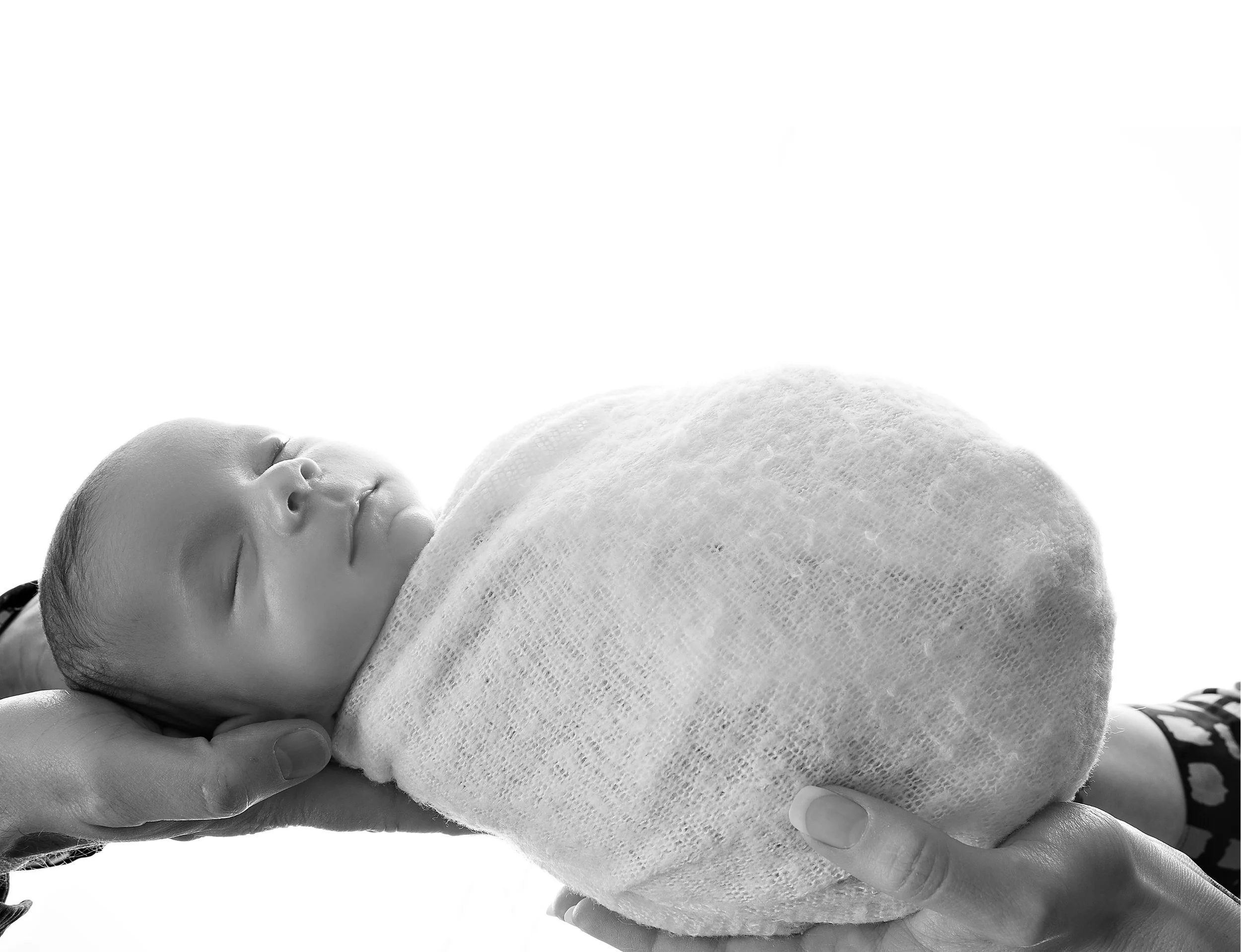 A newborn baby sleeping, being gently held and cradled in someone's hand, with a white blanket partially covering the baby.