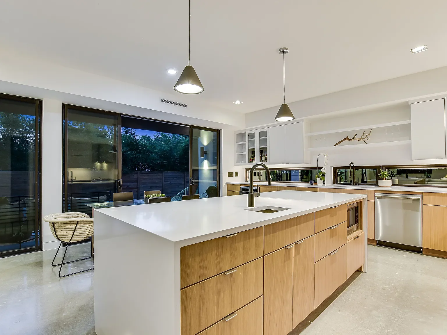Modern kitchen with white countertops, wooden cabinetry, large windows, and pendant lighting.