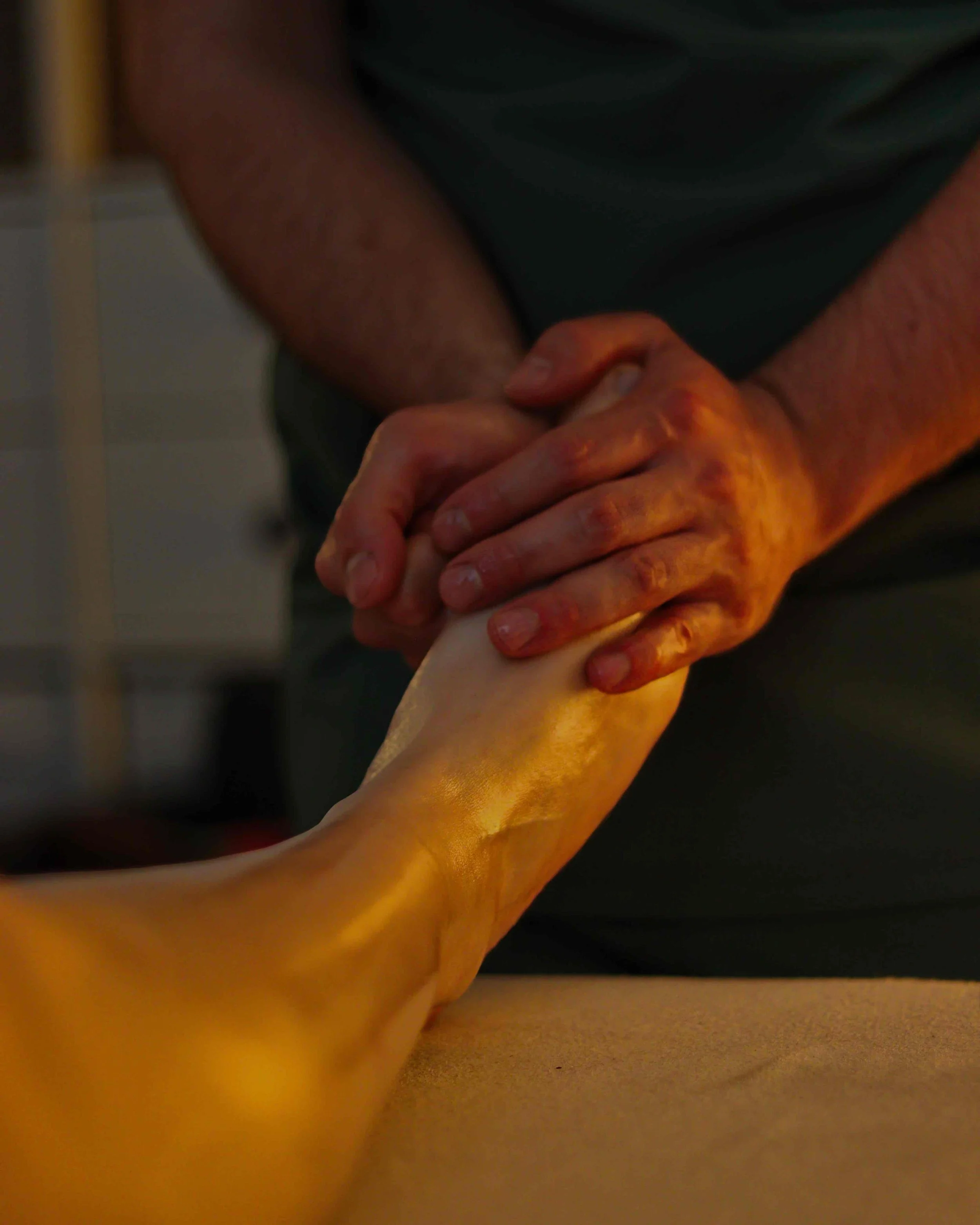 Close-up of hands holding a foot performing a foot reflexology treatment, foot massage, in a relaxing environment with welcoming ambient lighting.