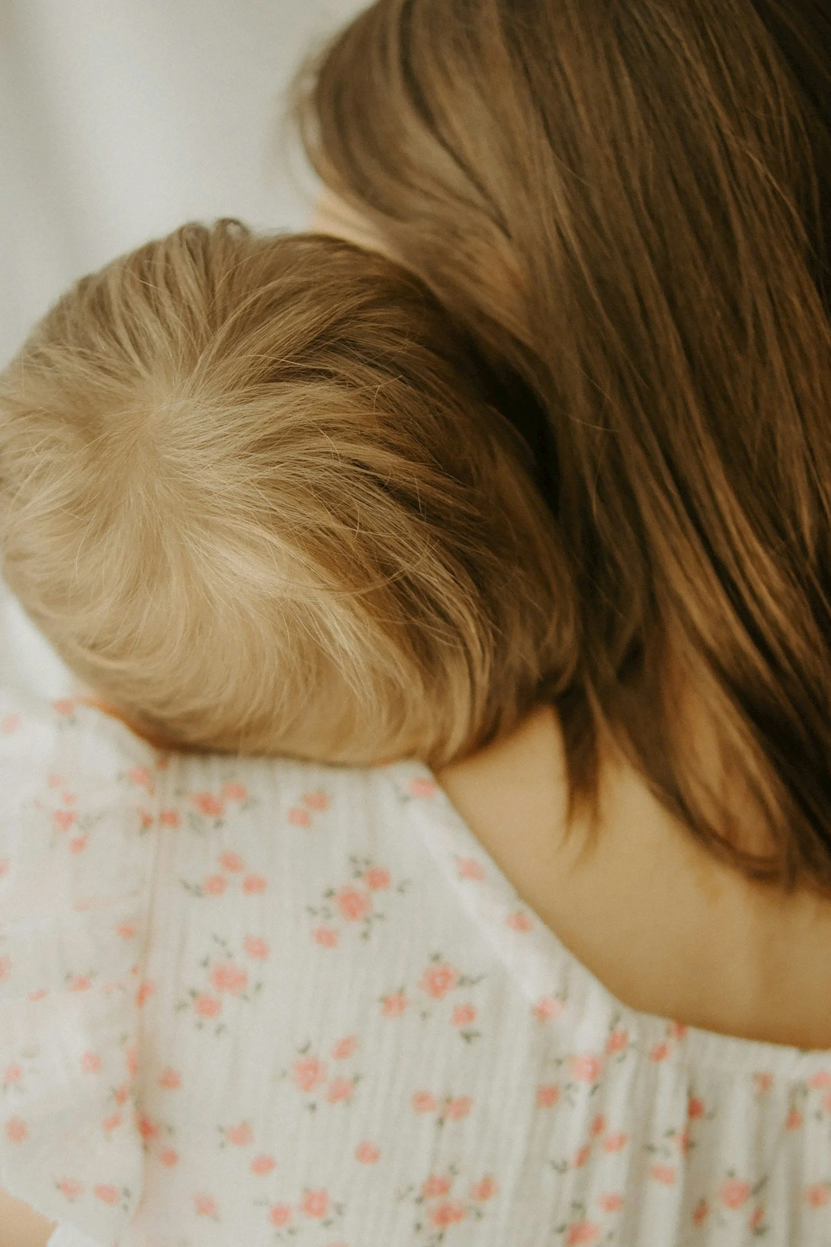 Young child with blonde hair sleeping on a bed, partially covered by a patterned white blanket with pink and peach flowers.