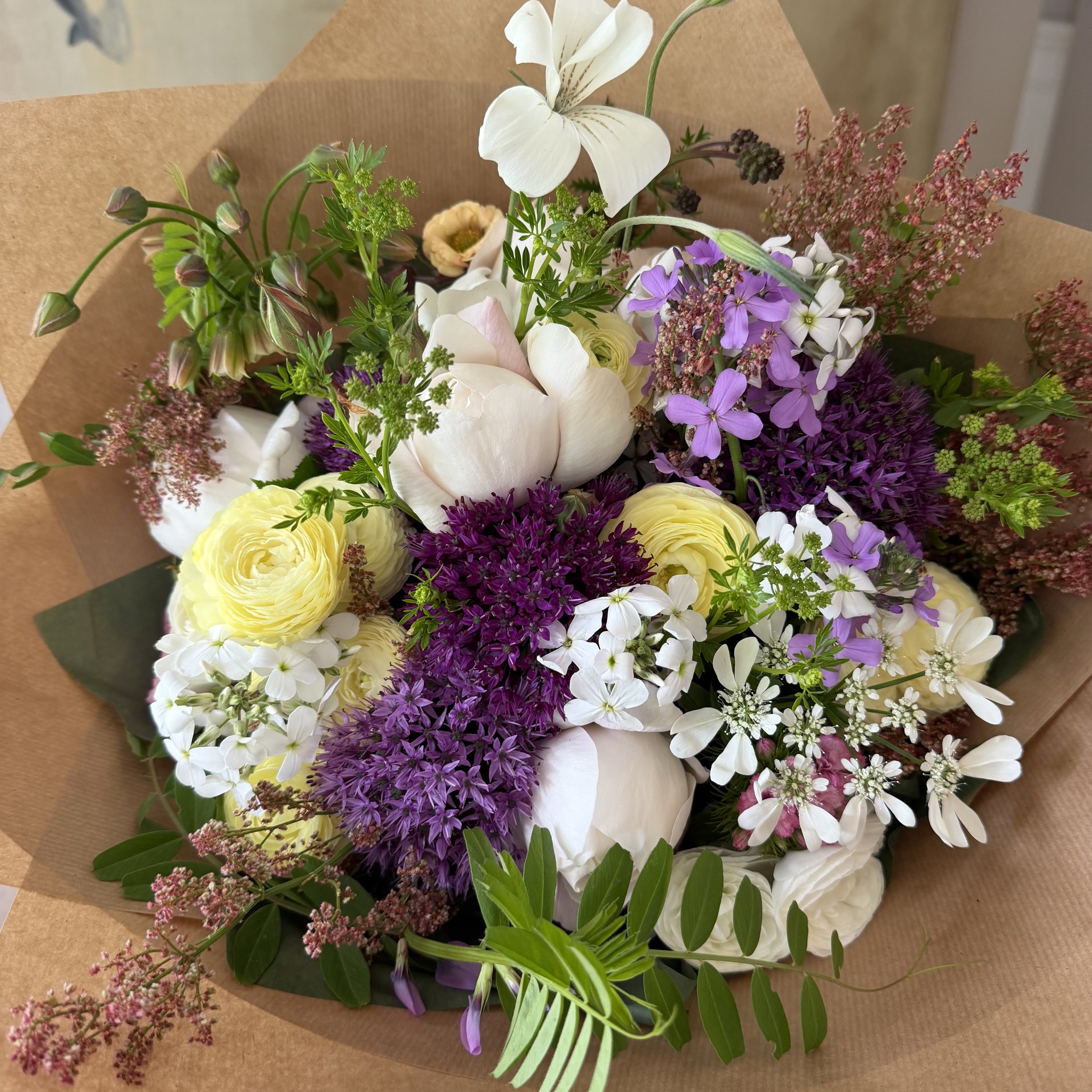 A colorful bouquet of mixed flowers including white, purple, and yellow blooms, wrapped in brown paper.