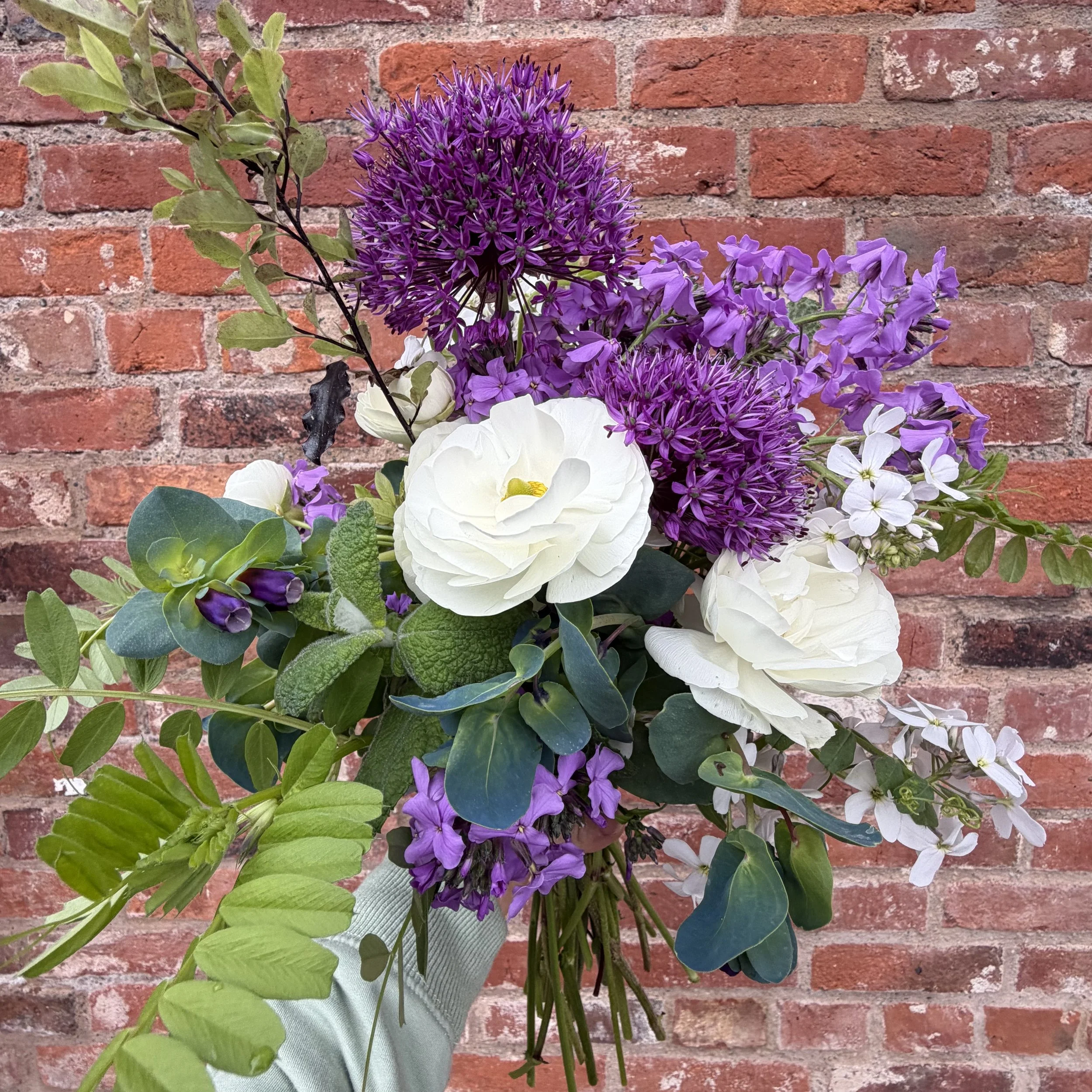 A bouquet of purple, white, and green flowers with a brick wall background.