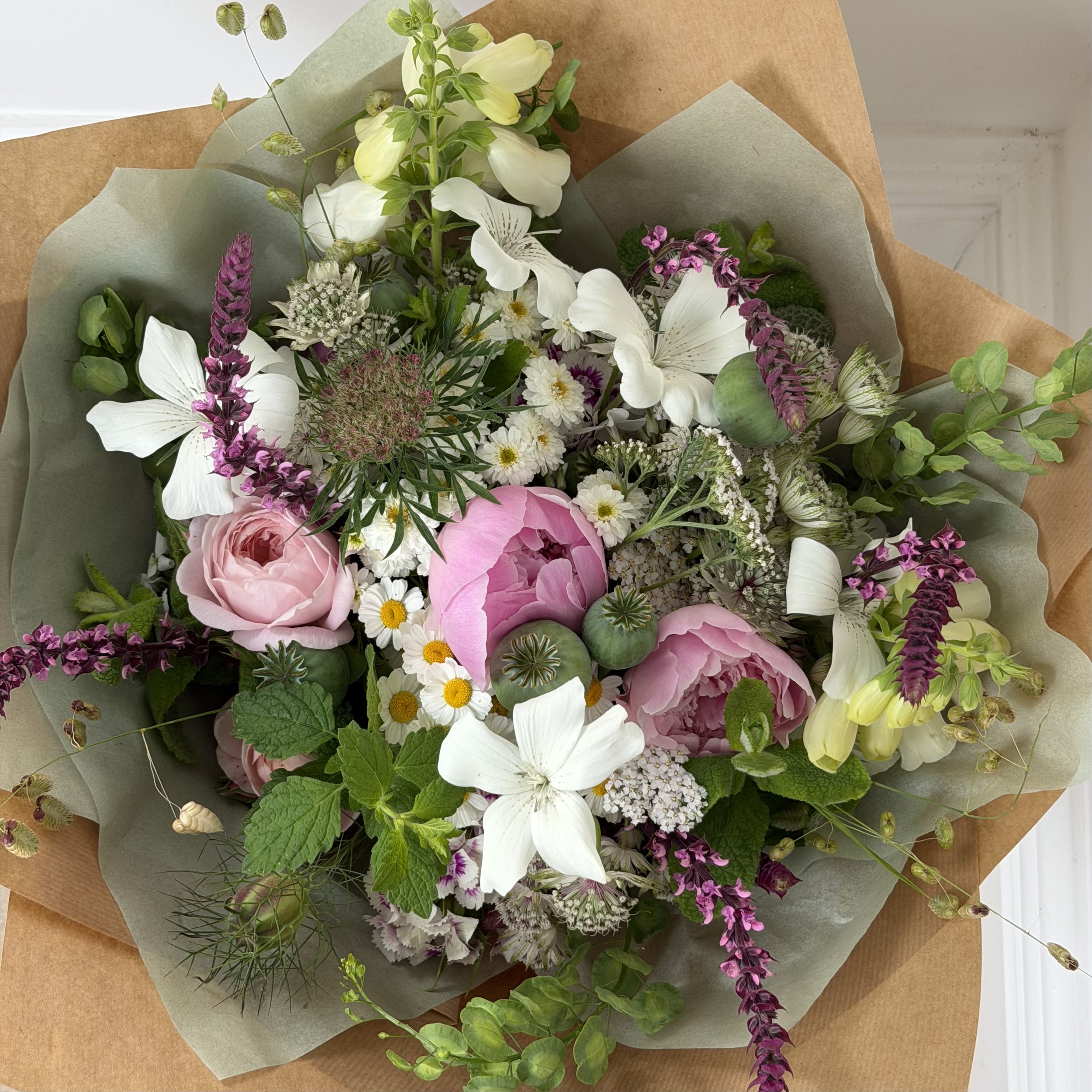 A bouquet of various colorful flowers wrapped in brown paper.